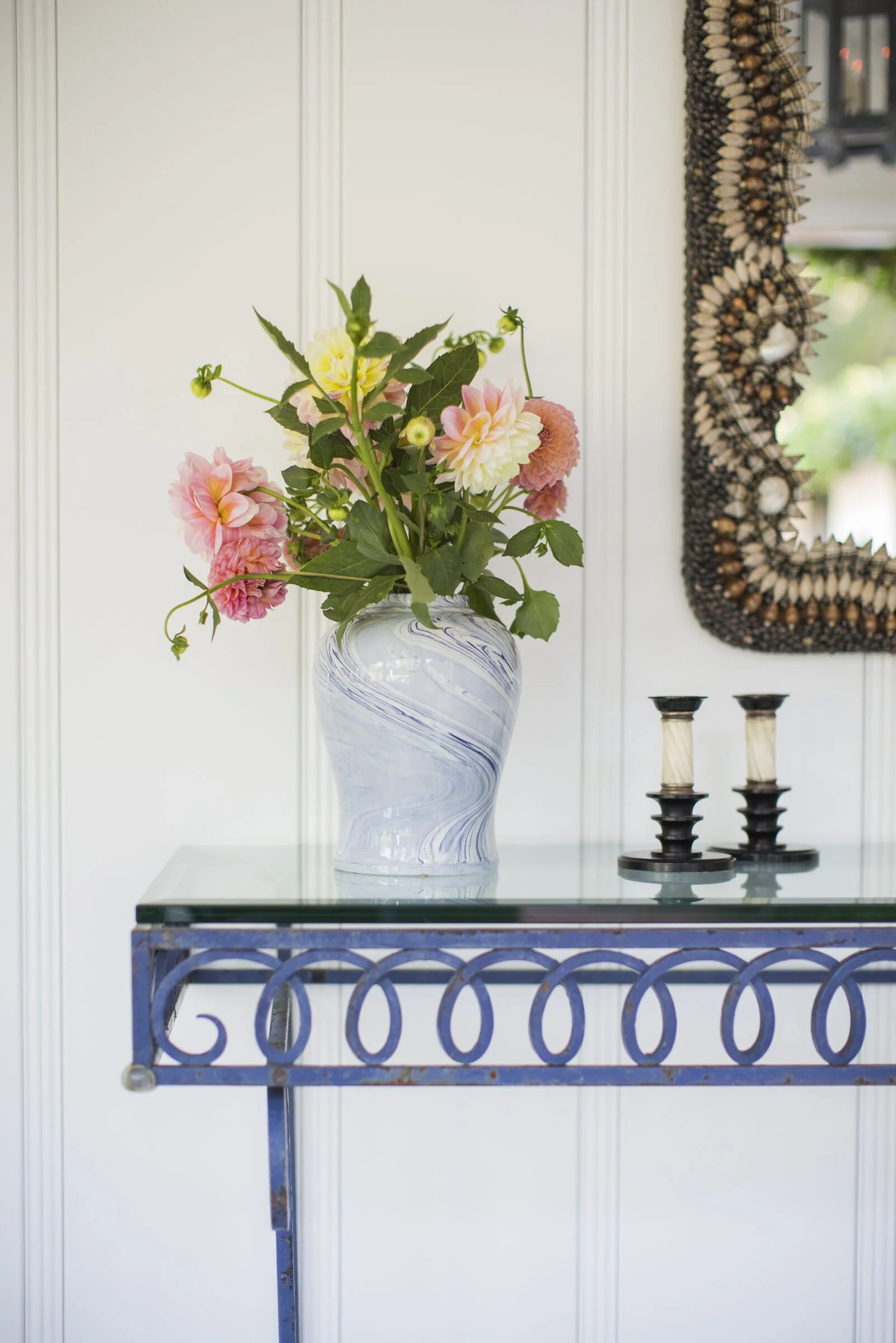 Marbleized blue-and-white vase of garden dahlias on a blue wrought iron console with a shell-encrusted mirror and two candlesticks
