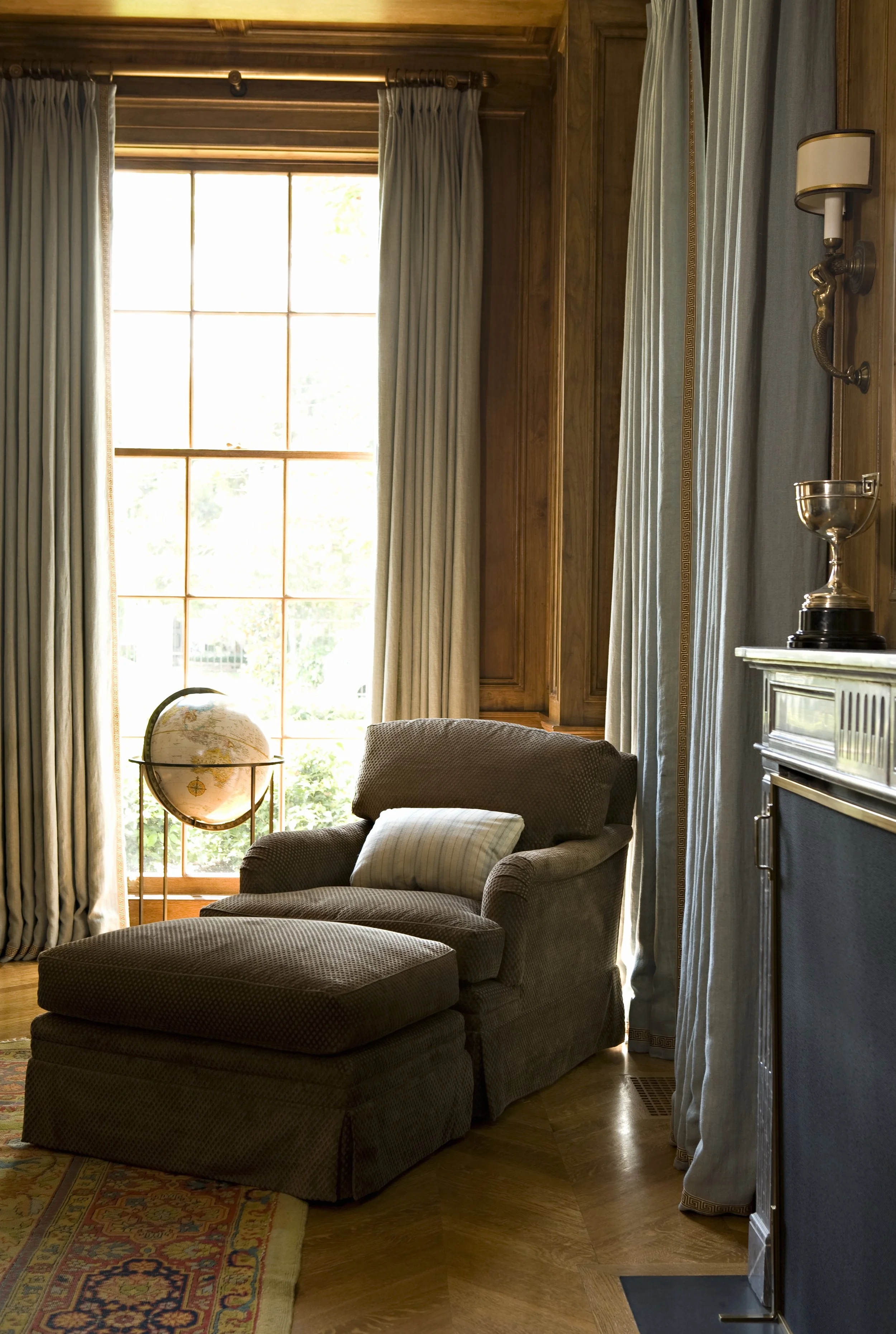 Wing chair, globe and trophy beside a window in the library