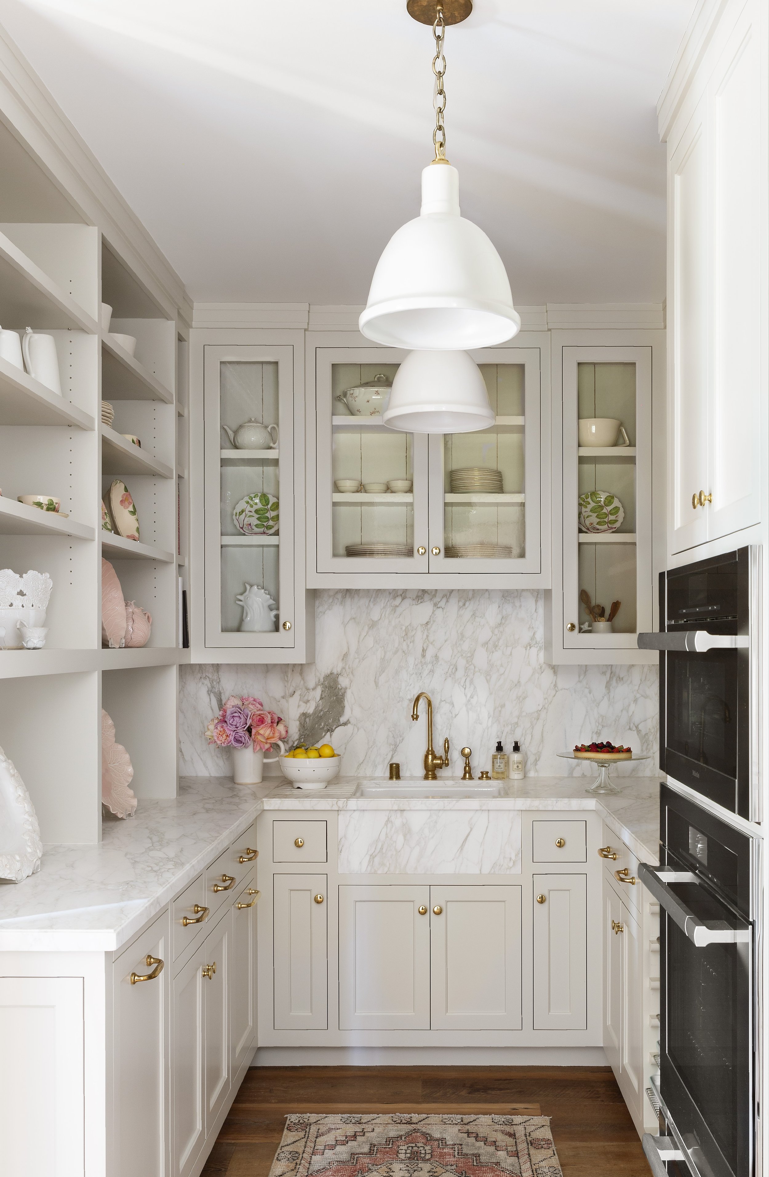Pantry with glass front cabinets, marble backsplash and a brass faucet
