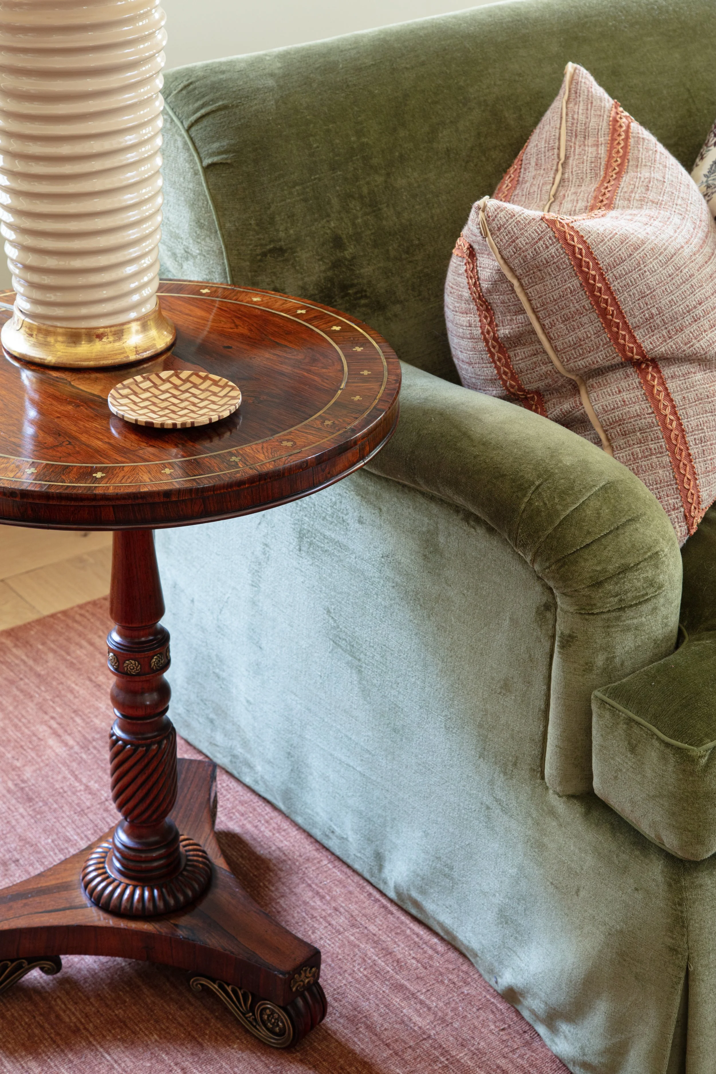 Round mahogany side table with inlay beside a moss green velvet chair and a striped pillow