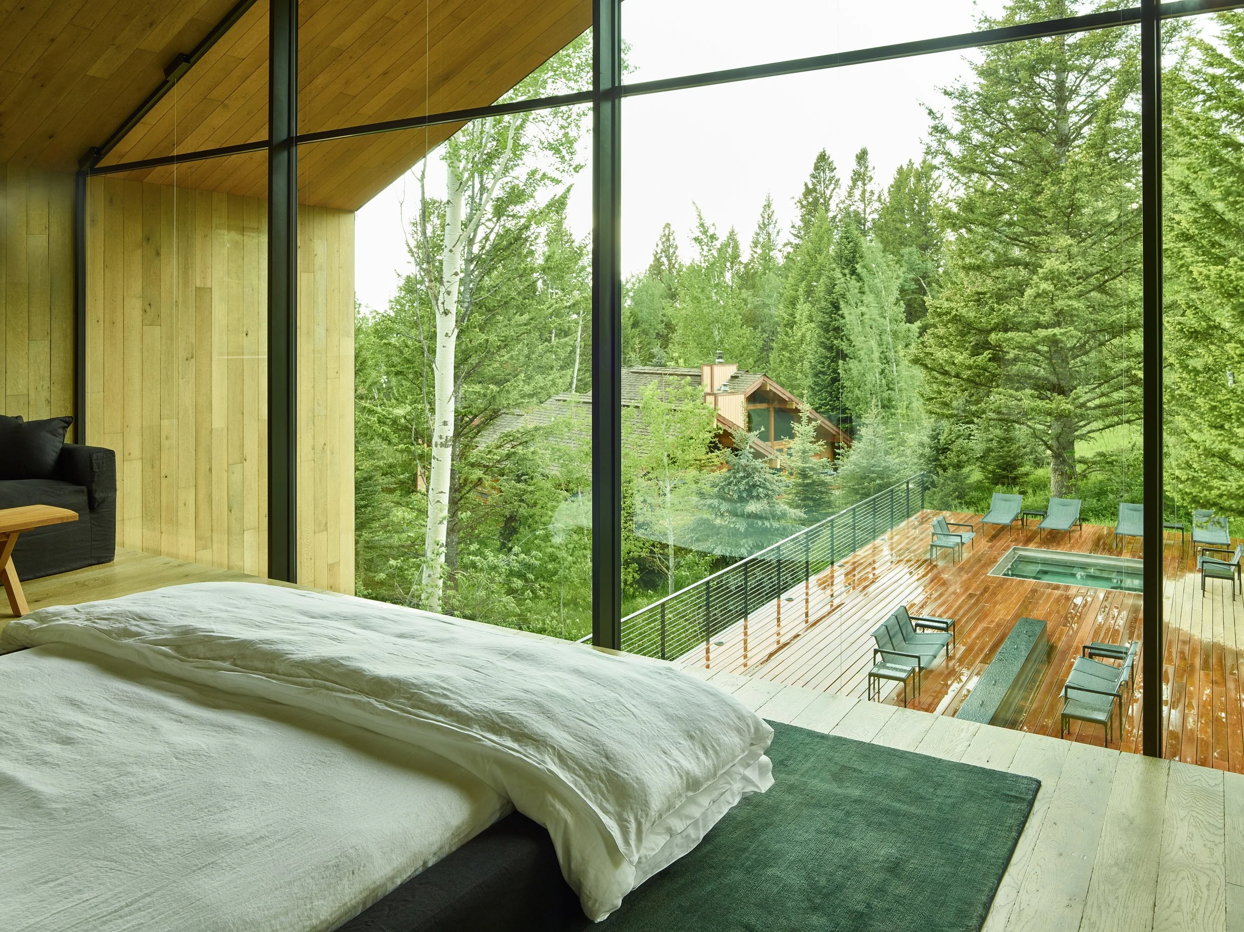 Bedroom with floor to ceiling glass overlooking the forest and a deck below