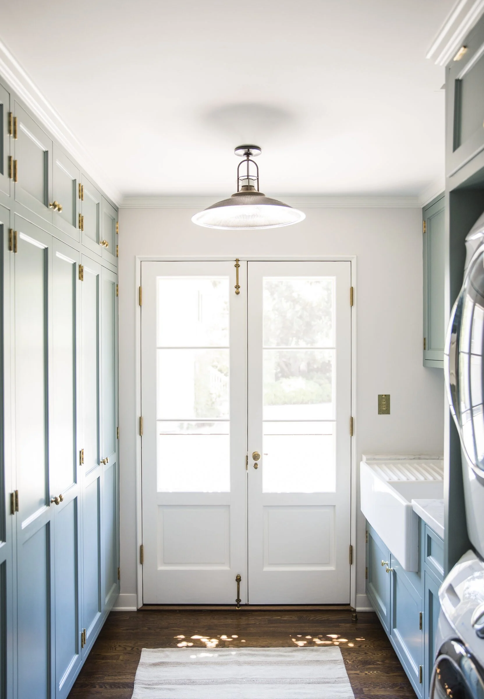 Back hall with blue painted built-in cabinets, brass hardware, a farmhouse sink and white French doors leading to the garden