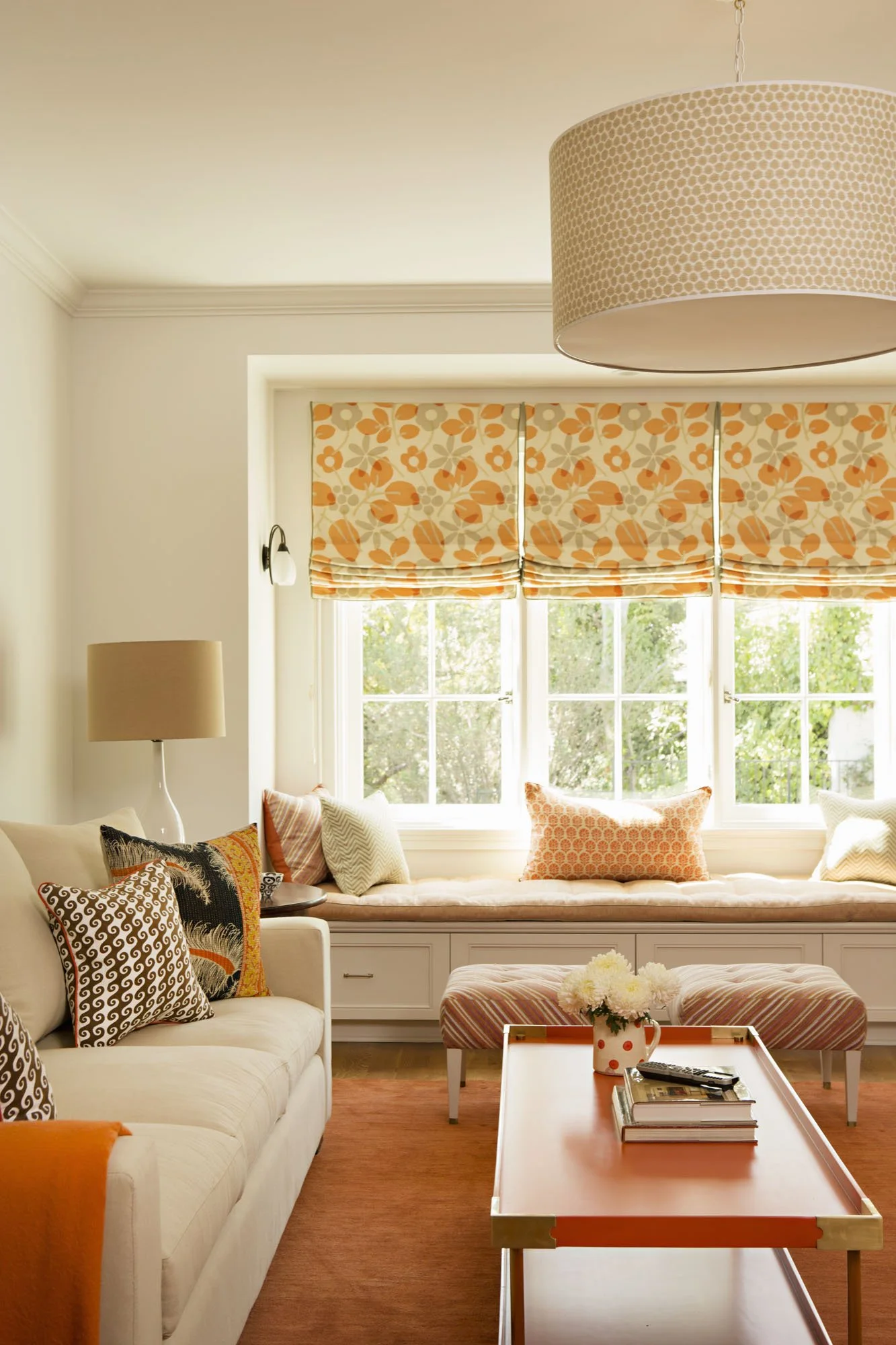 Window seat with an orange floral roman shade and patterned pillows