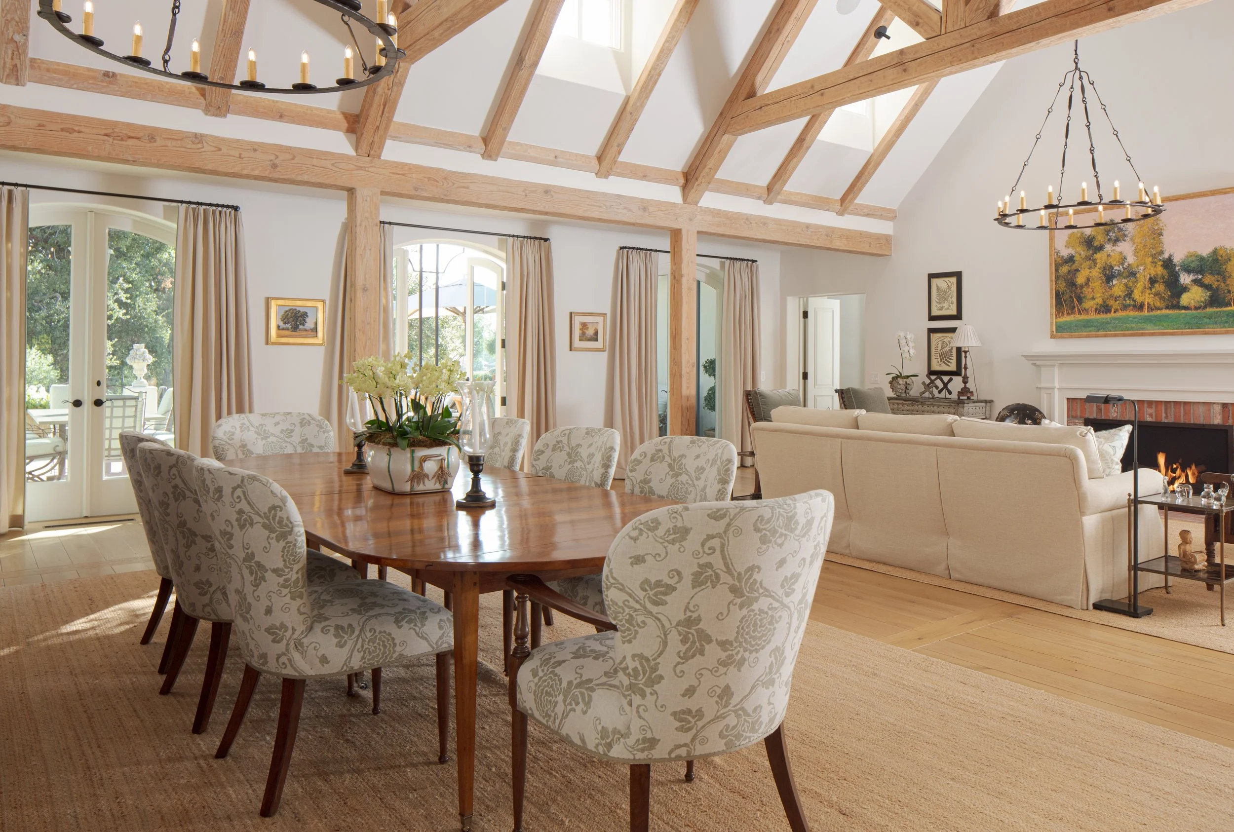 Vaulted dining and living area with exposed timber beams, a round table with patterned chairs and a chandelier