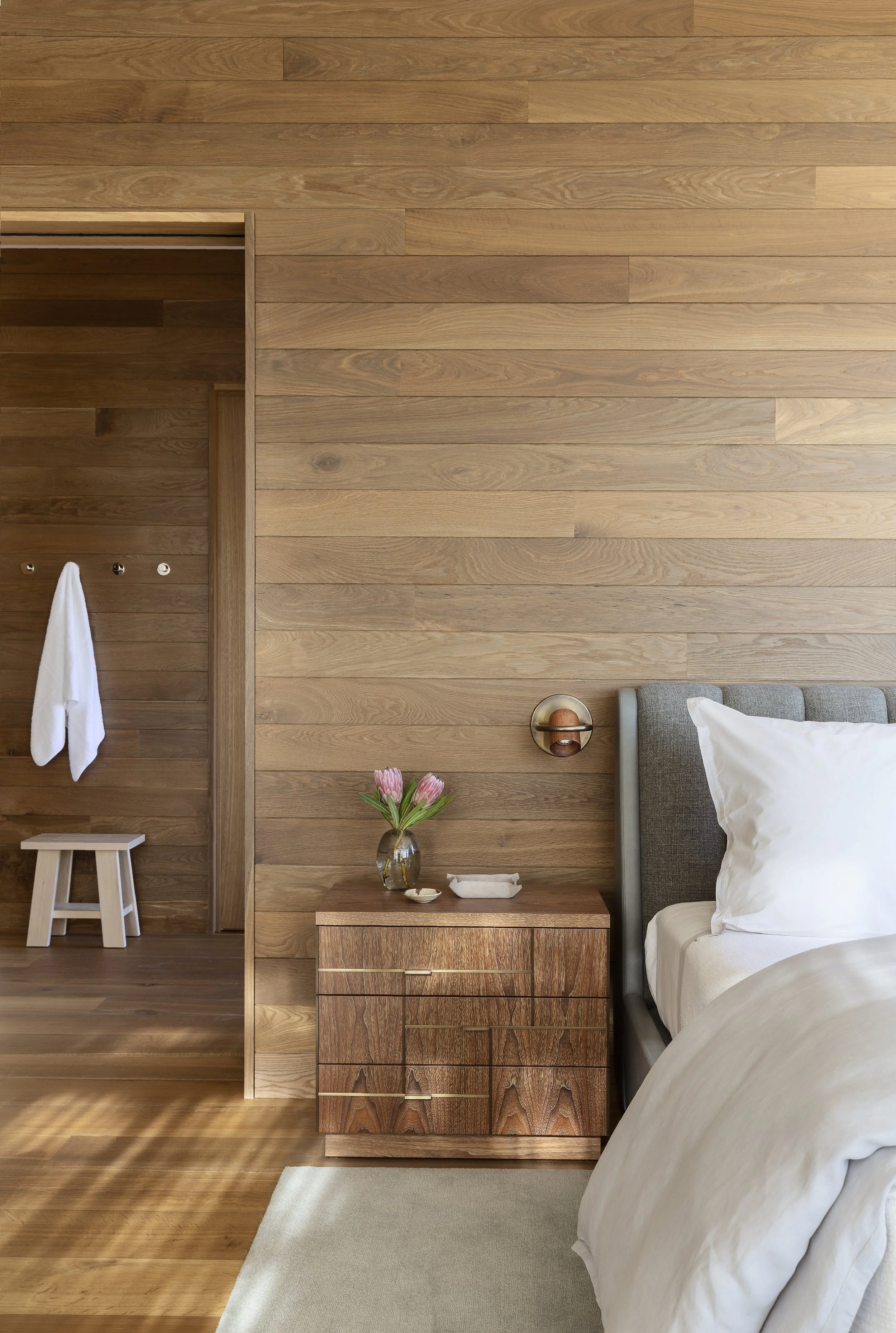 Bedroom with white oak wall paneling, a wood stool and a gray upholstered headboard