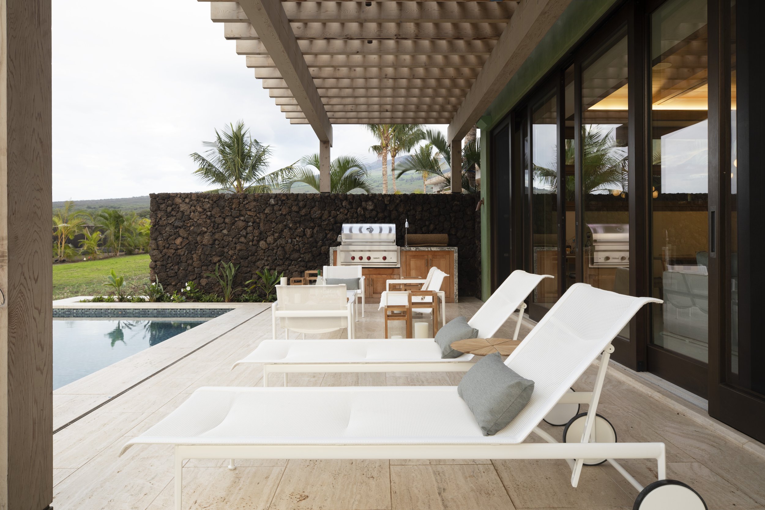 Poolside lounge chairs and outdoor kitchen beneath a pergola