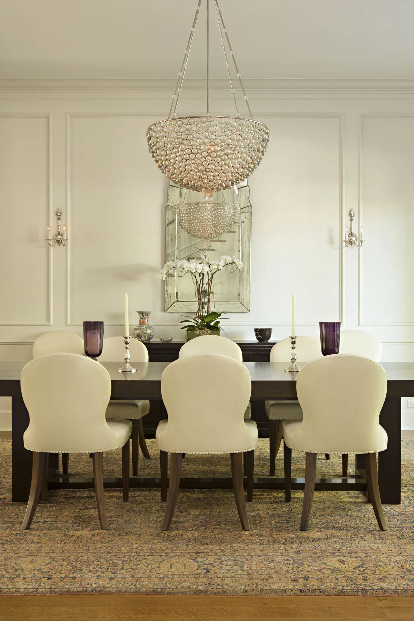 Dining room with white chairs, dark table, mirror and shell chandelier