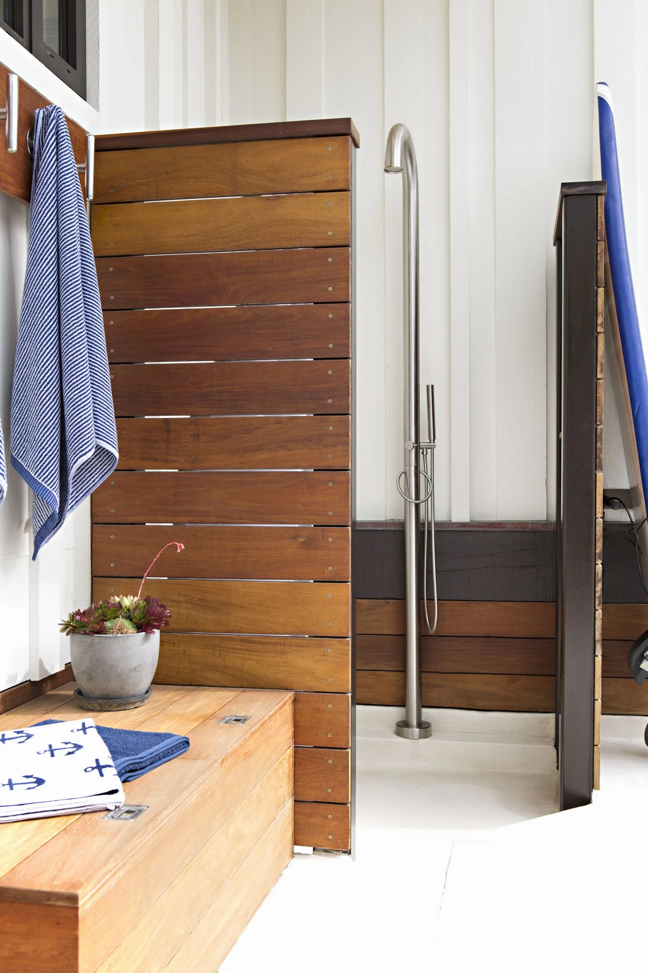 Outdoor shower with a teak slat screen, a blue striped towel and a potted succulent