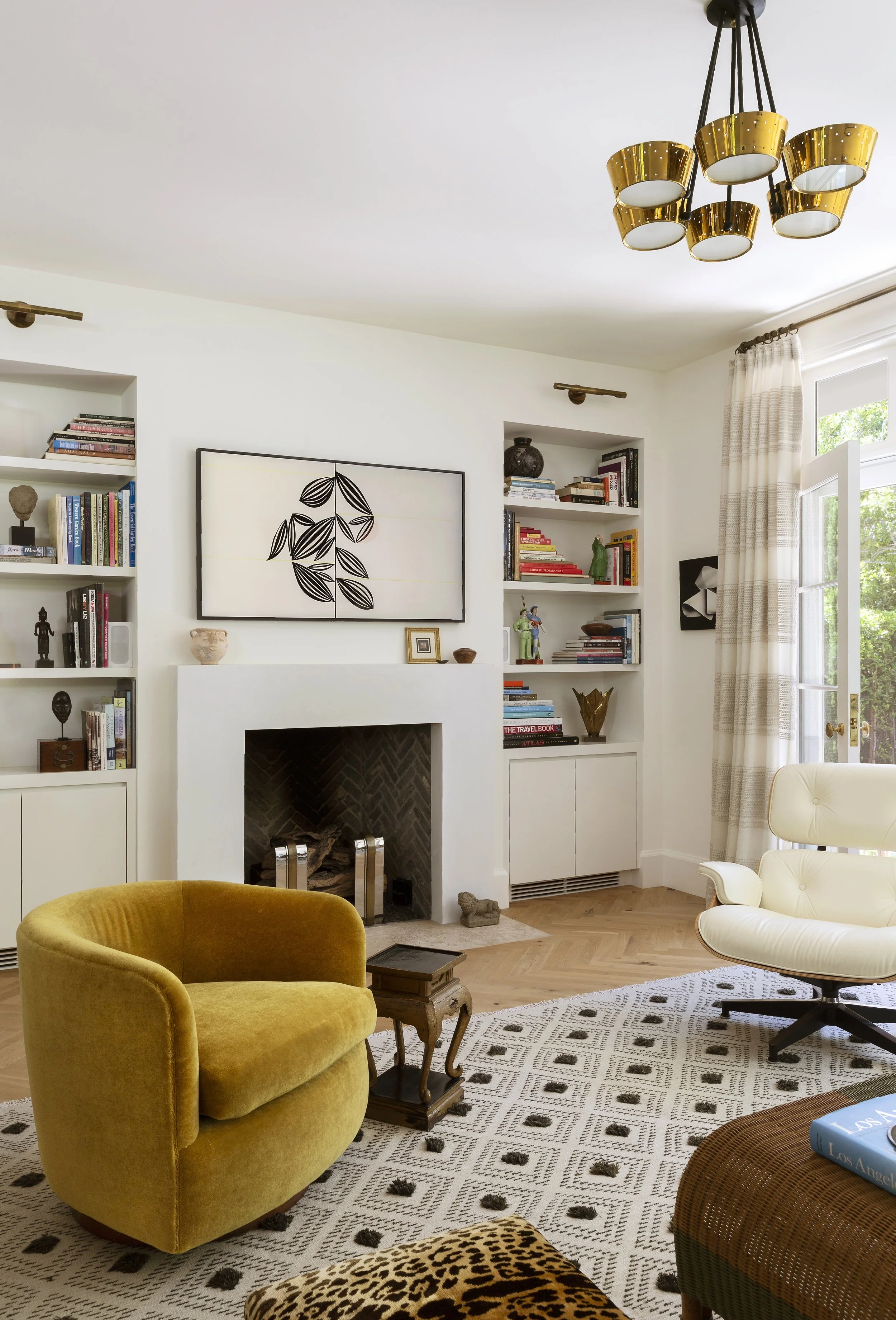 Living room with a white fireplace, built-in bookshelves, mustard velvet chair and botanical art