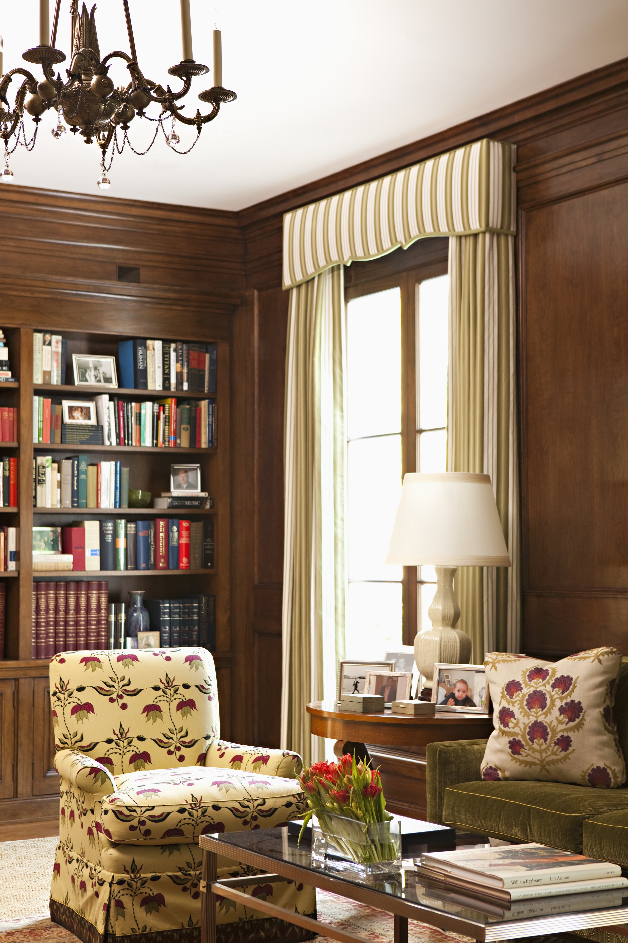 Library shelves filled with books beside striped curtains and a table lamp