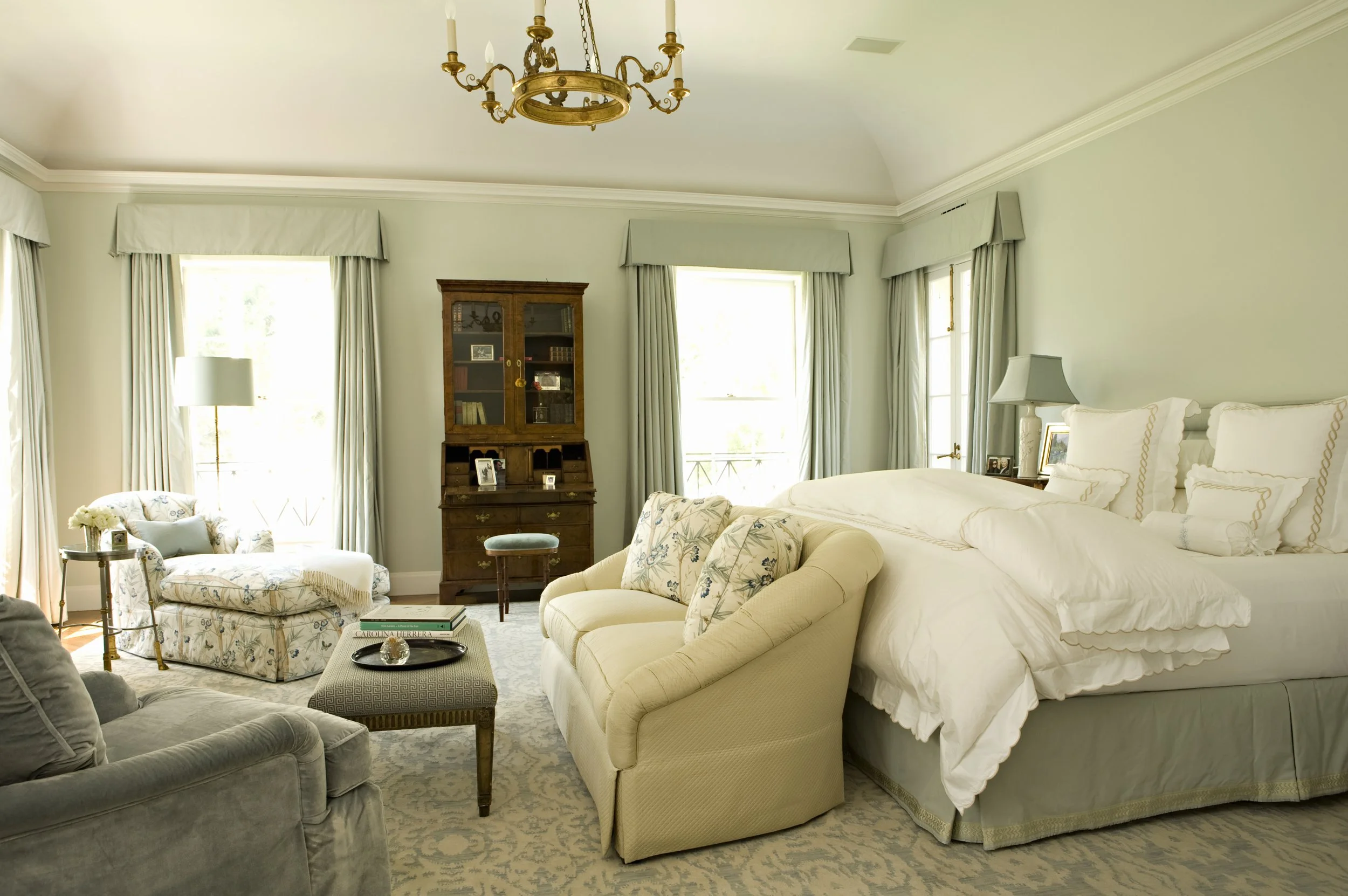 Primary bedroom in soft gray green with a cream sofa, bookcase and tall windows