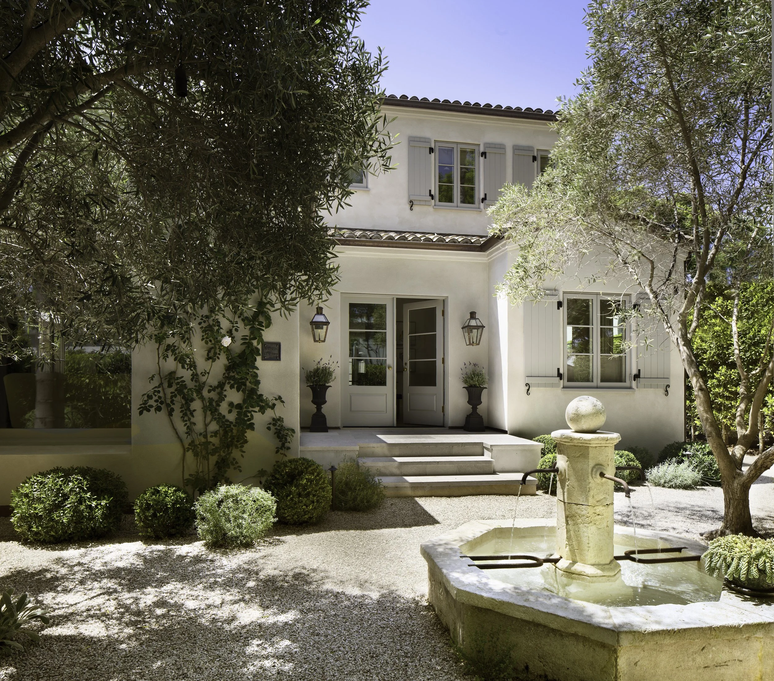 Whitewashed house with olive trees, a stone fountain and a gravel courtyard