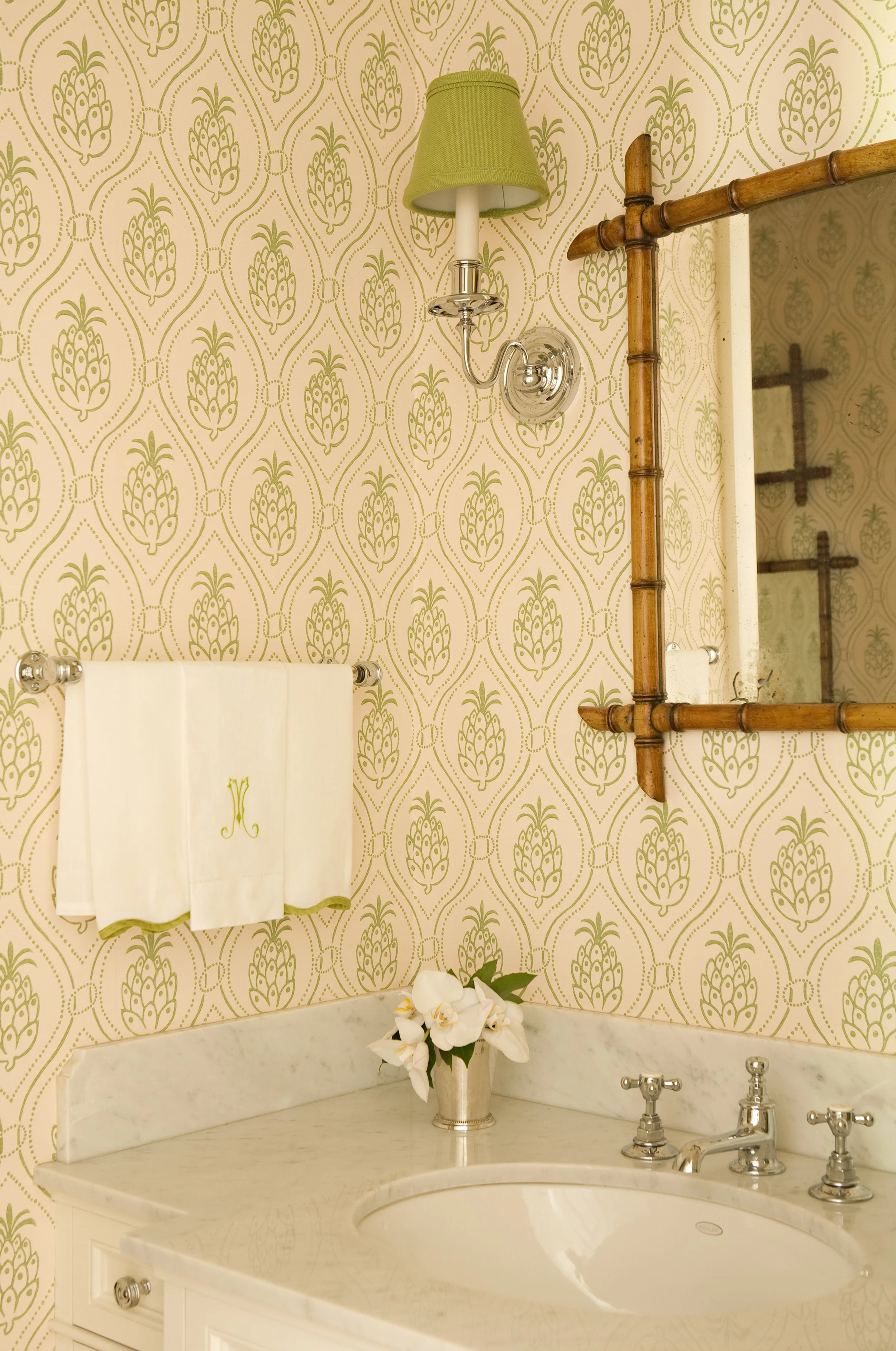 Bathroom with pineapple wallpaper, a bamboo mirror and a monogrammed towel