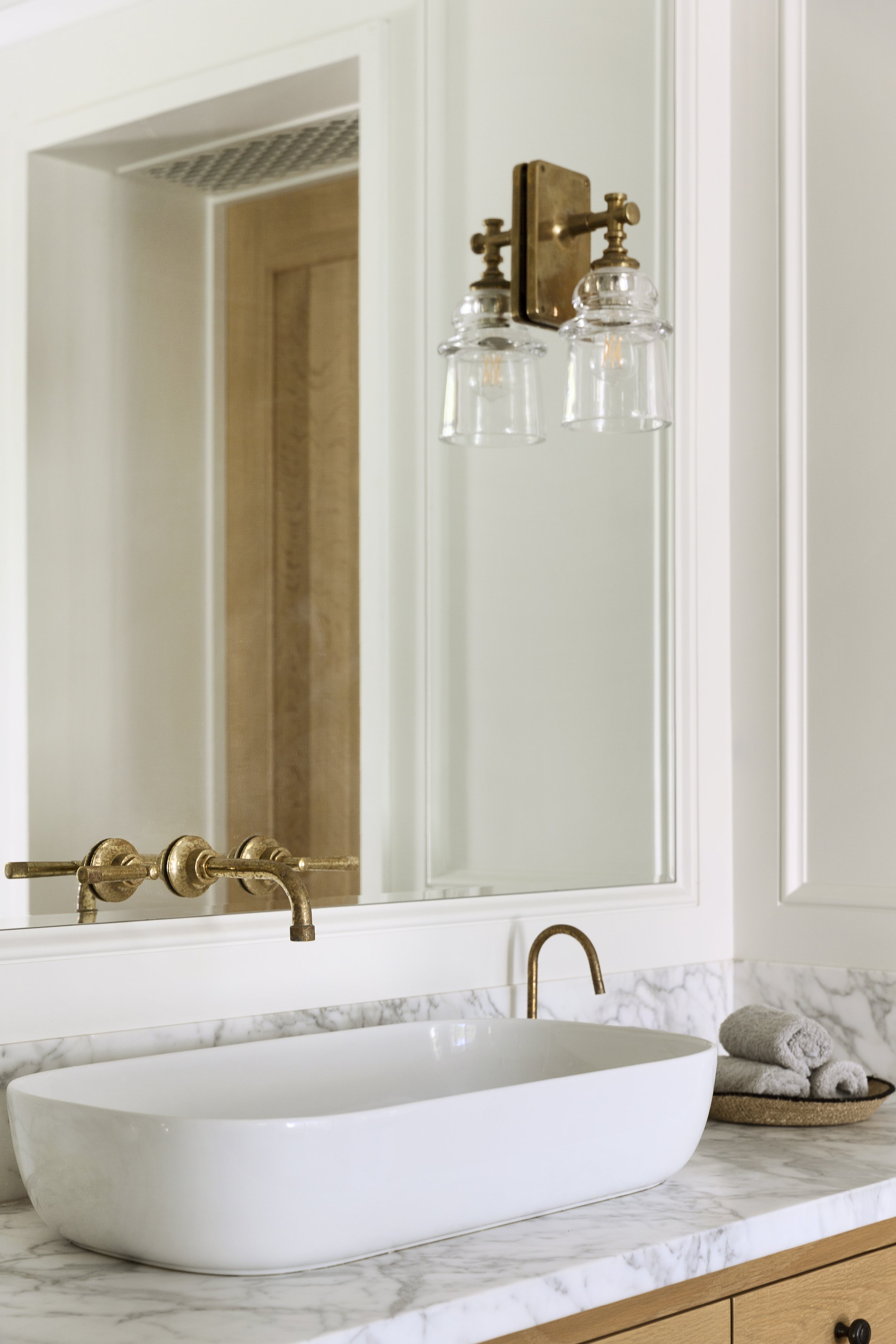 Brass wall mounted faucet at a mirrored vanity