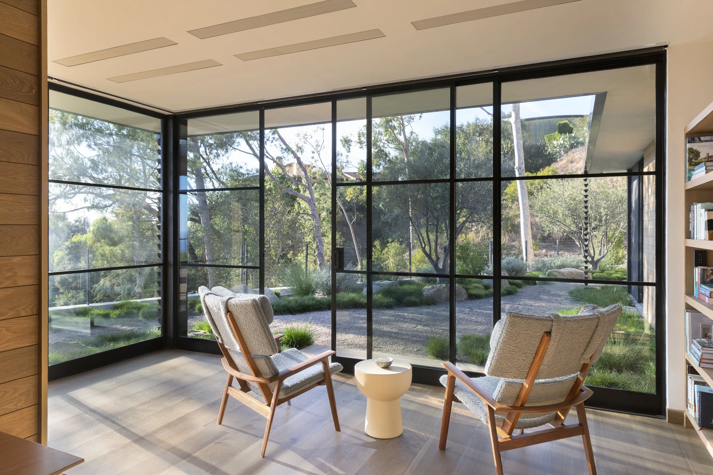Sunroom lined with steel-framed glass, two leather sling chairs and a stone side table