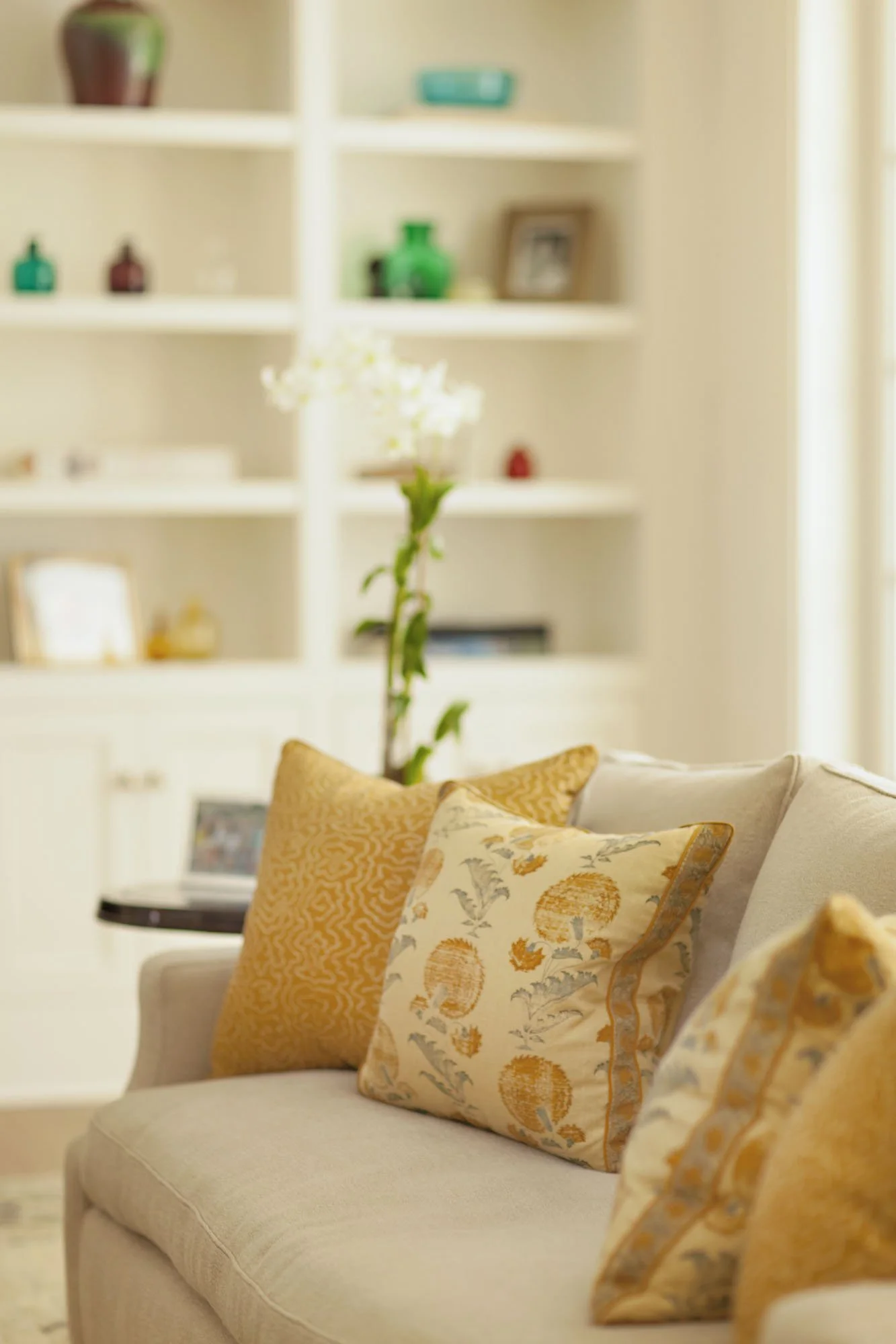 Cream sofa with gold floral pillows in front of built-in shelving