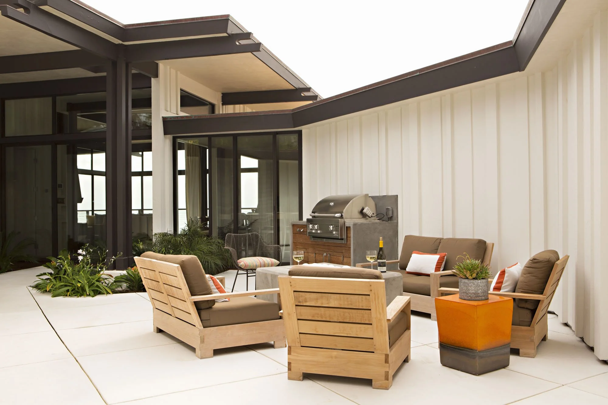 Courtyard patio with teak lounge chairs, orange side tables and a built-in grill under a dark overhanging roof