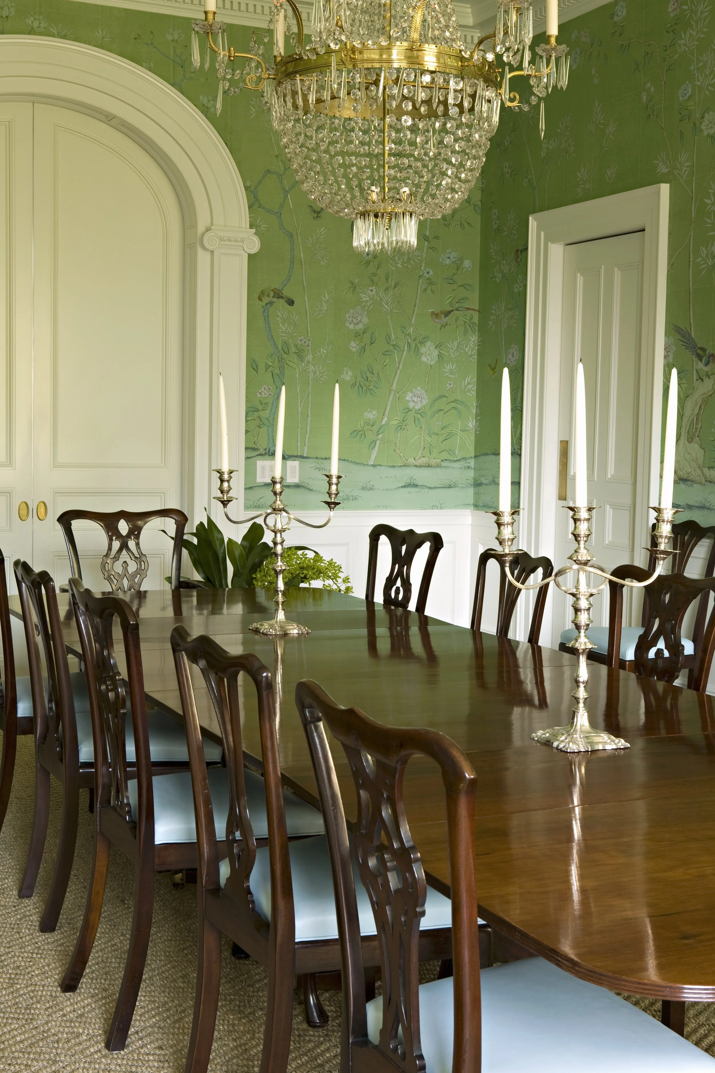 Dining table set with silver candelabra beneath green chinoiserie wallpaper