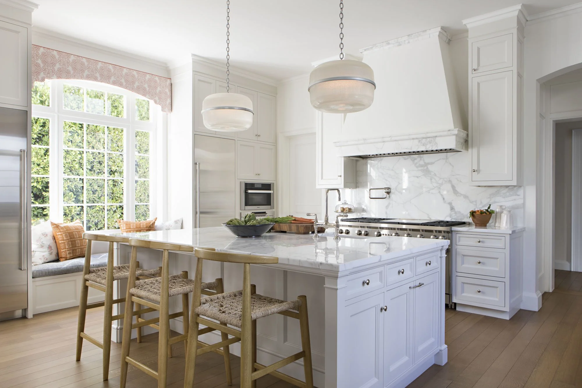 White kitchen with marble island, wood and rattan counter stools and a pair of pendant lights