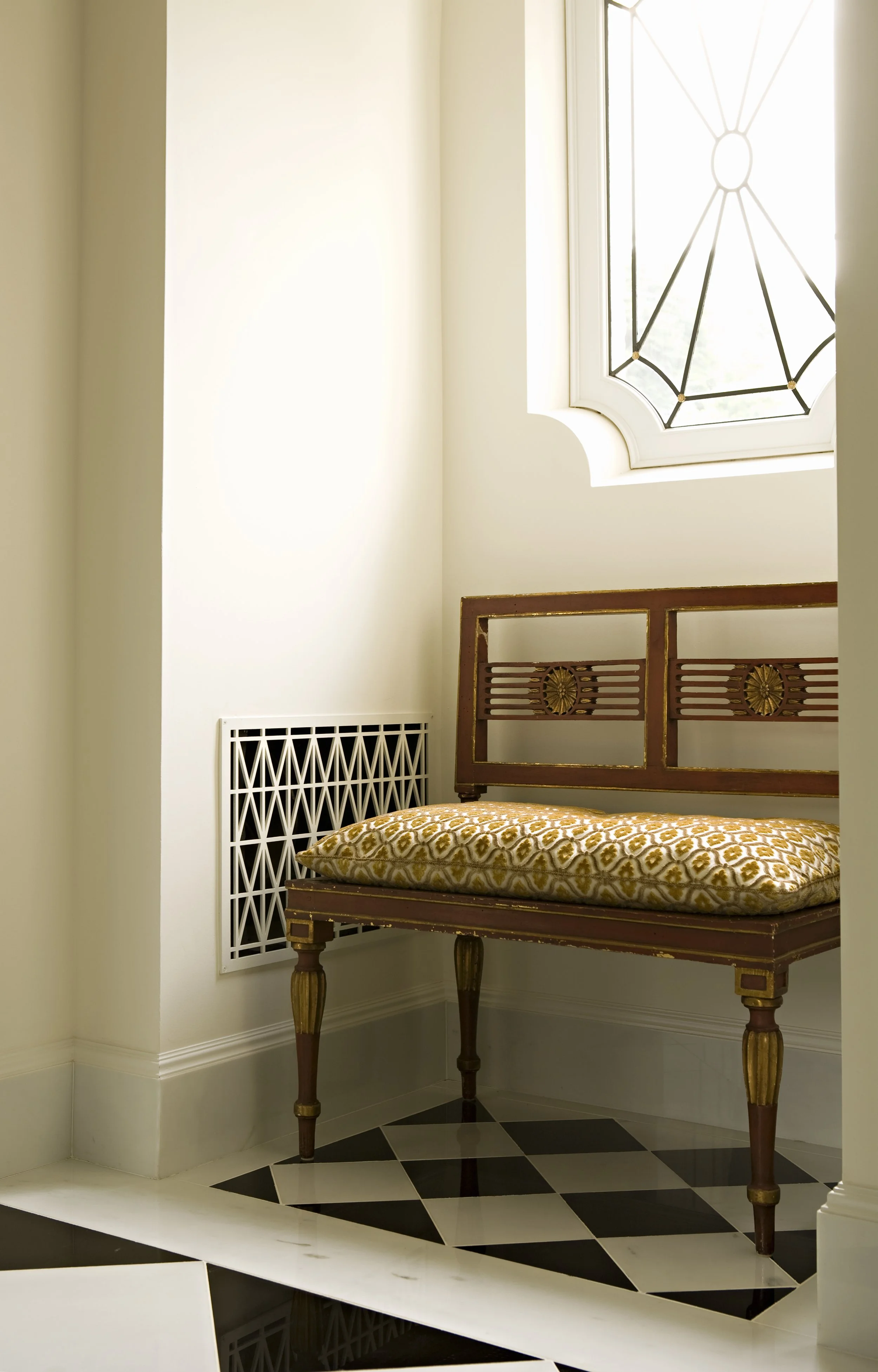 Entry nook with a carved wood bench, yellow cushion and a lattice radiator cover