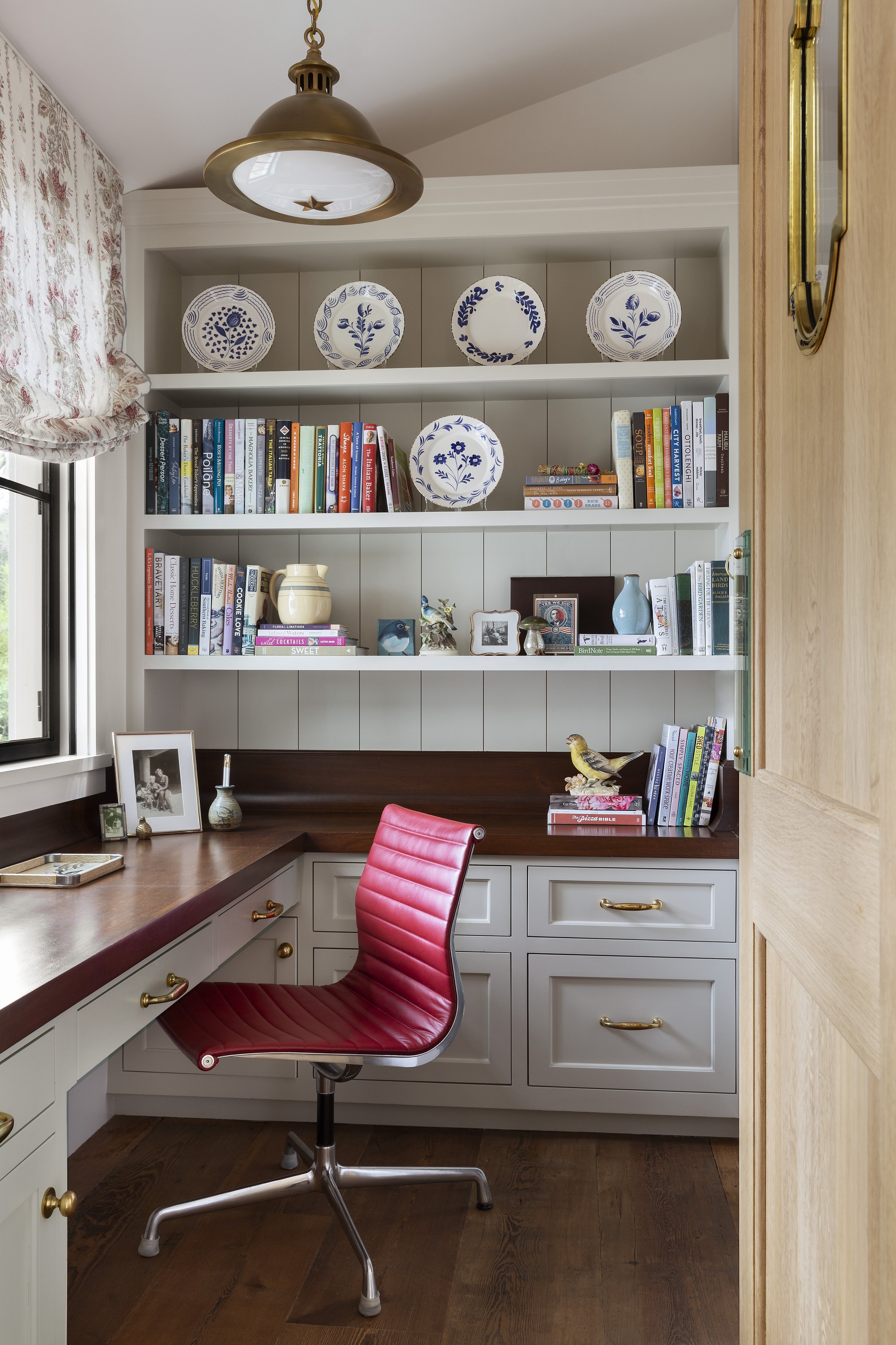Home office with built-in shelves, a red leather chair and a desk by the window