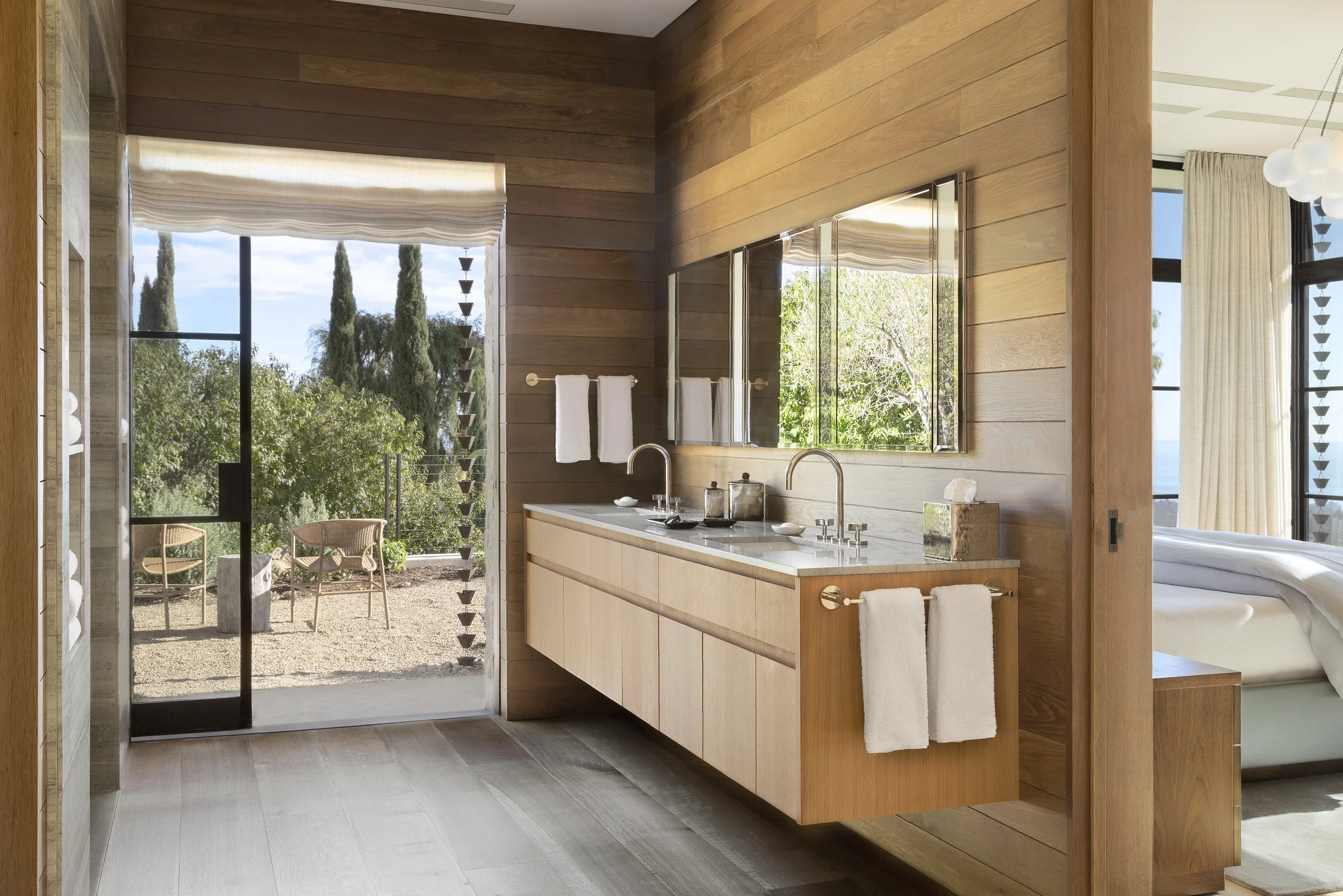 Bath with a floating oak vanity and a glass door opening to an olive garden