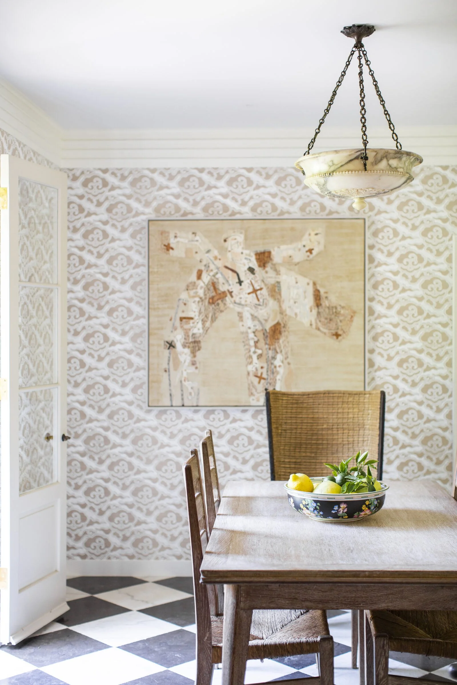 Breakfast room with cloud-pattern wallpaper, an abstract painting, a rustic wood table with a bowl of lemons and a black-and-white checkered floor