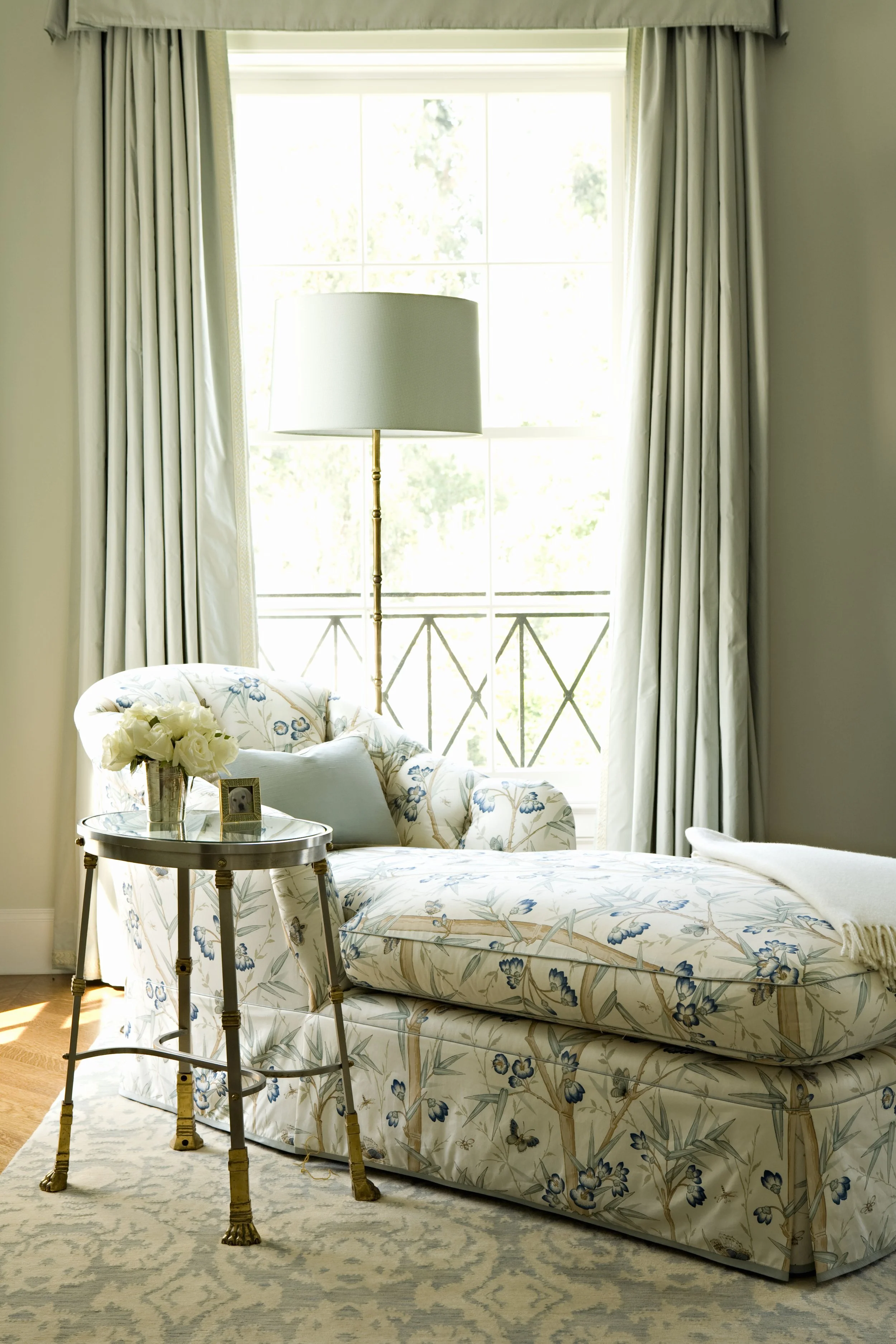 Chaise in blue floral fabric before a balcony door with gray green drapes
