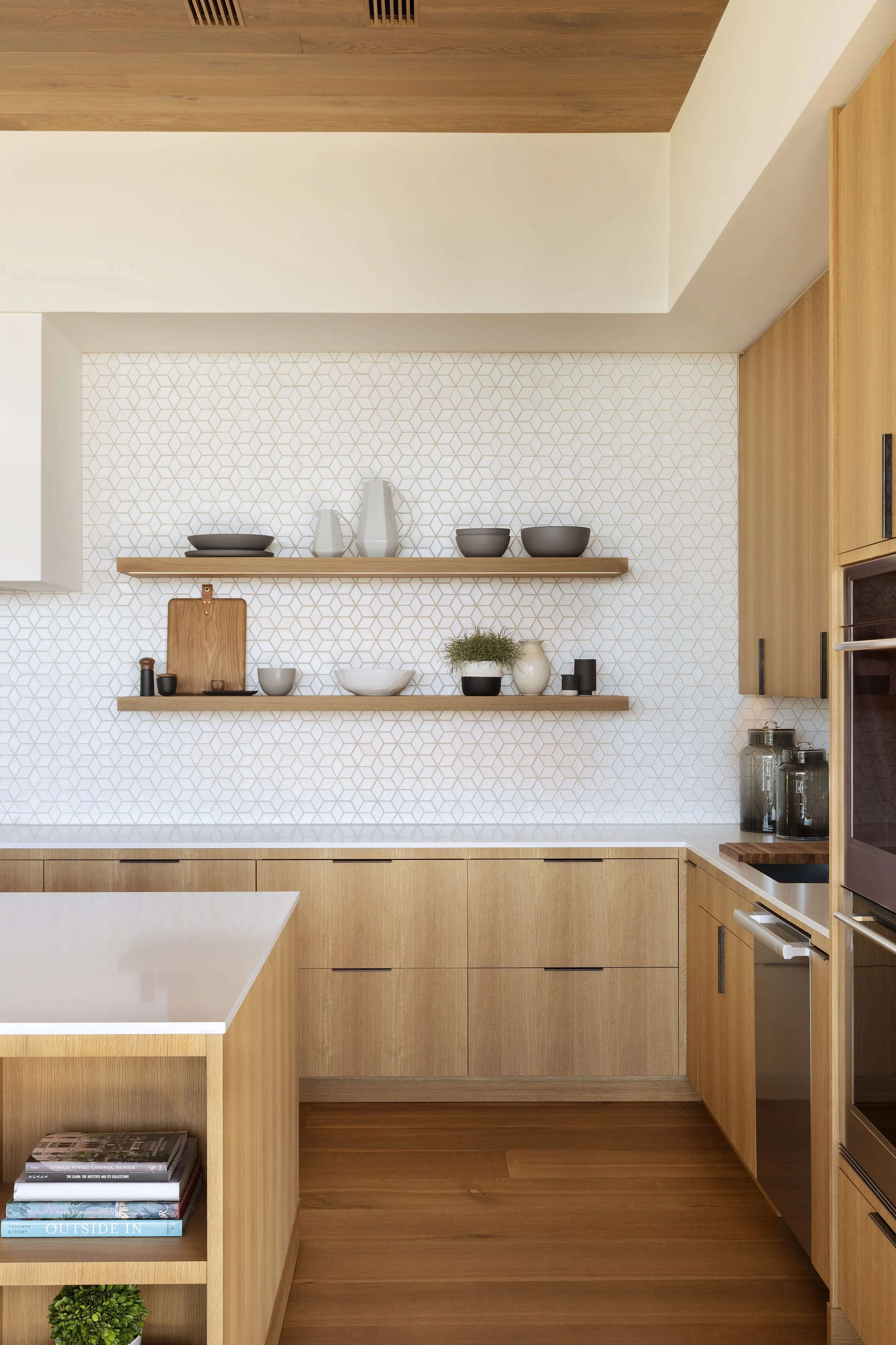 Kitchen shelves with a white hex tile backsplash above oak cabinets