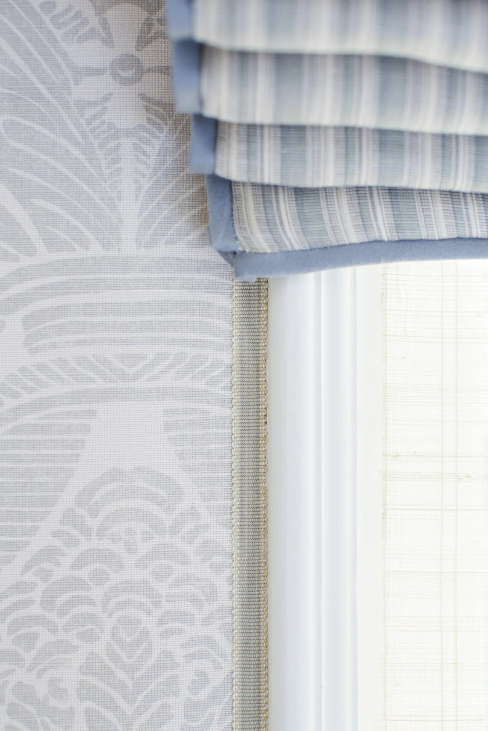 Close view of gray patterned wallcovering beside a blue striped Roman shade with a blue border