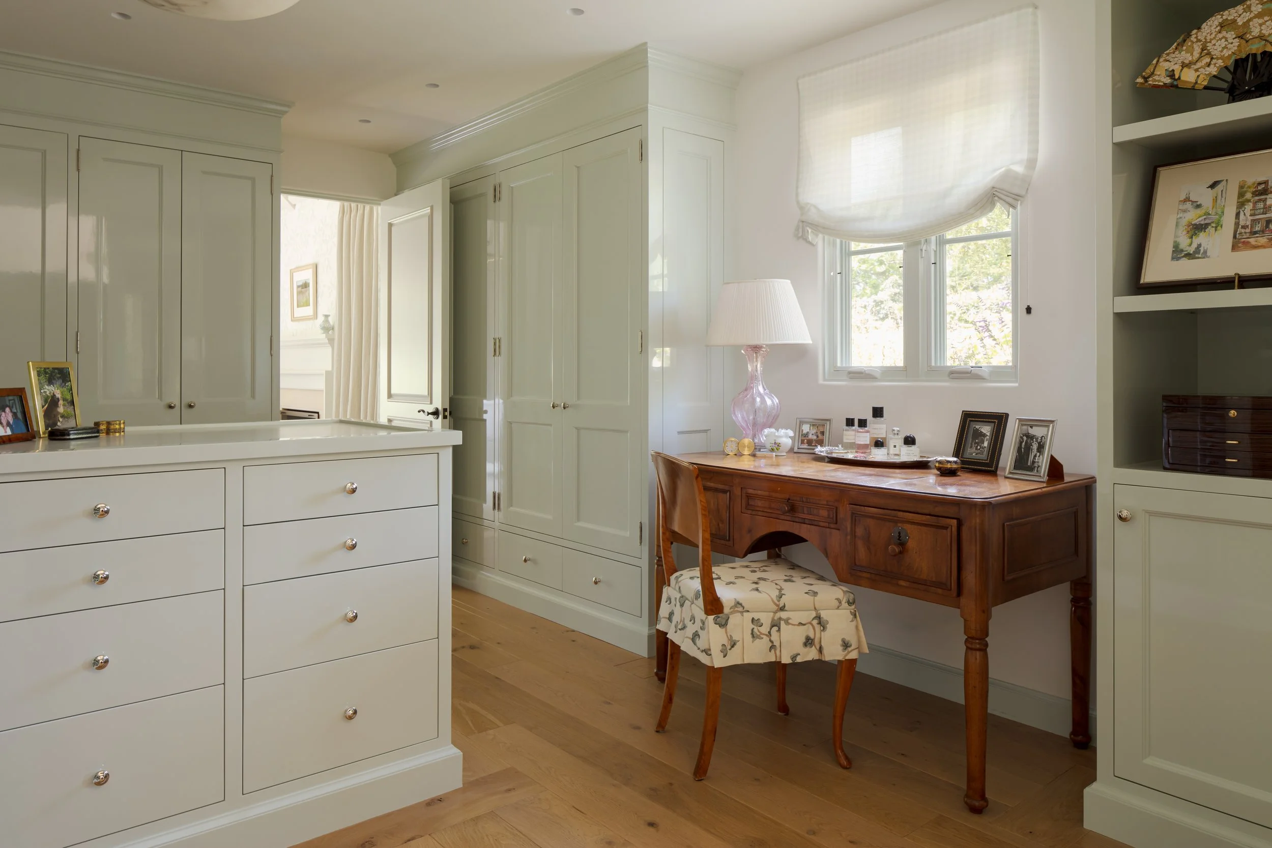 Dressing room with pale green built-in cabinetry, a wood writing desk and a floral upholstered stool