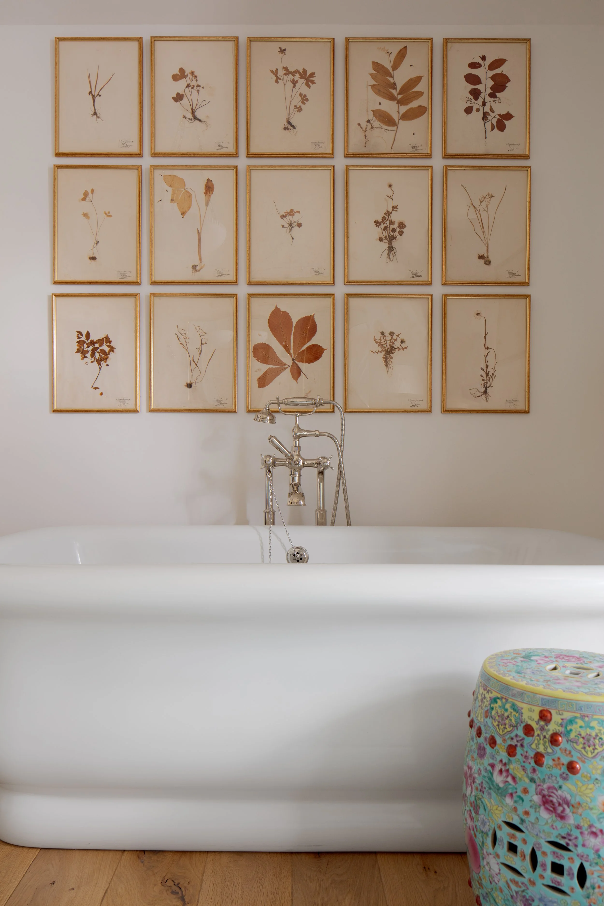 Freestanding white tub with a polished nickel filler beneath a grid of framed pressed botanical prints