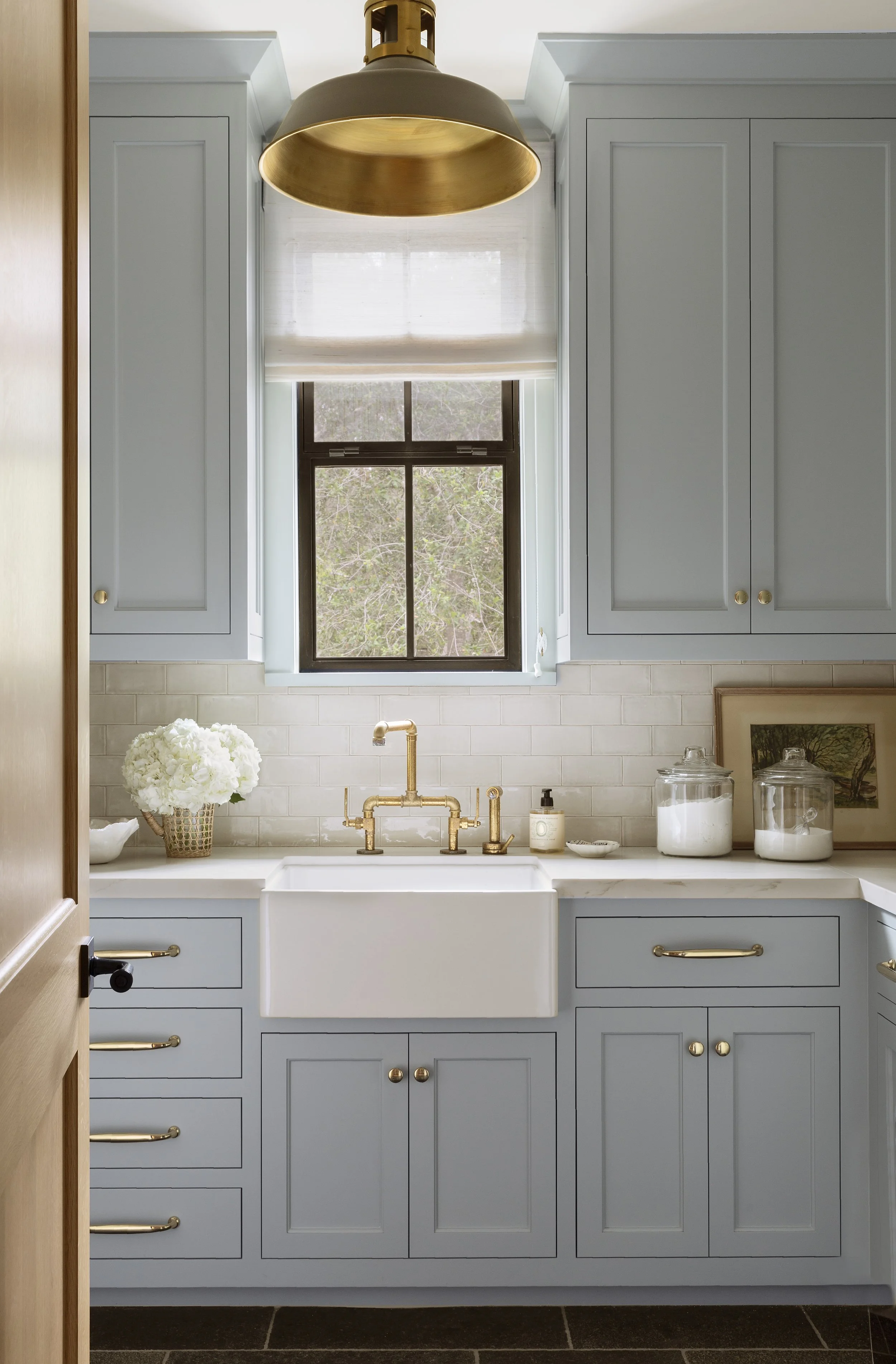 Laundry room with blue-gray cabinets, farmhouse sink and brass faucet
