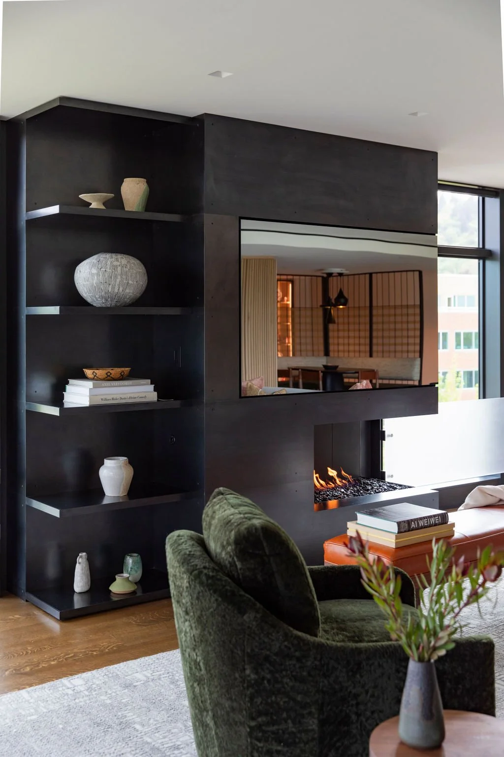 Dark steel shelving with ceramics, a see-through fireplace and a green velvet chair