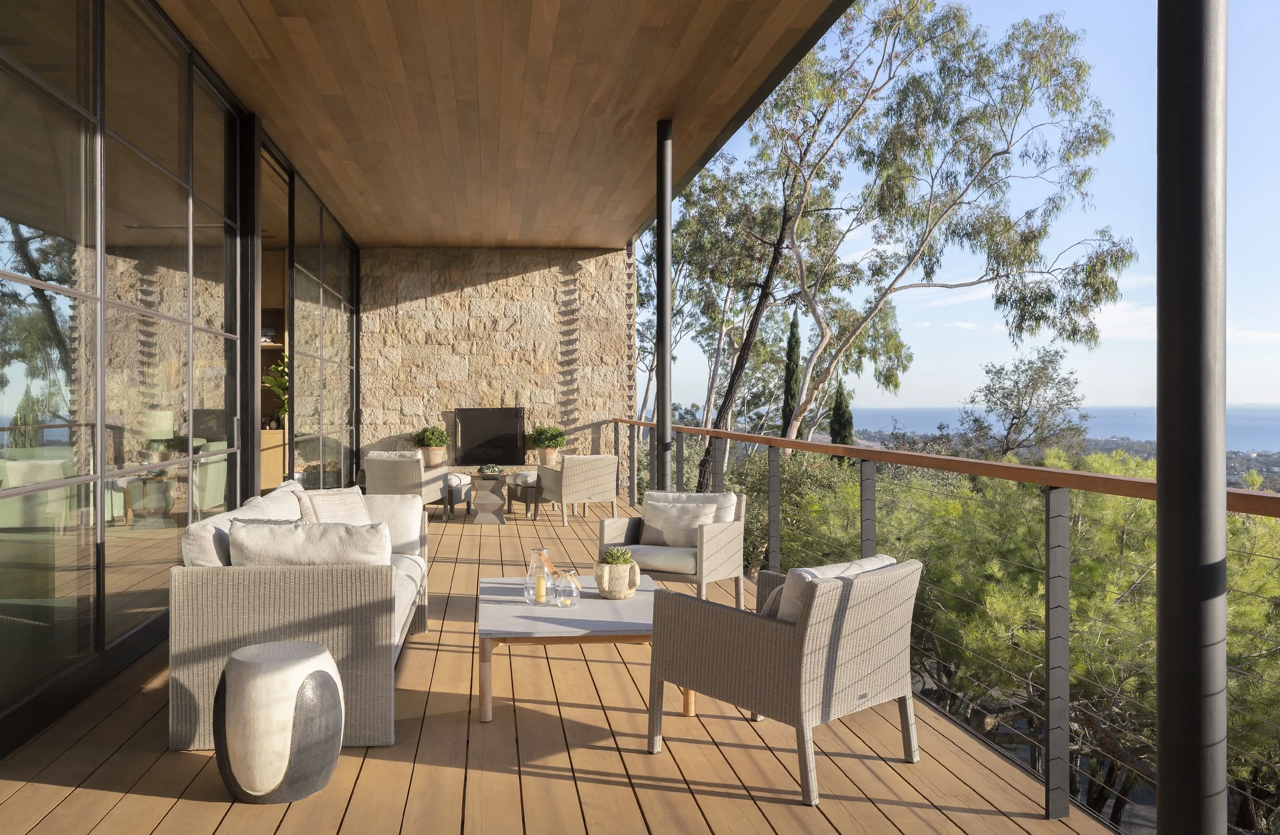 Covered terrace with wicker seating and a wood ceiling, with a view over the treetops to the ocean