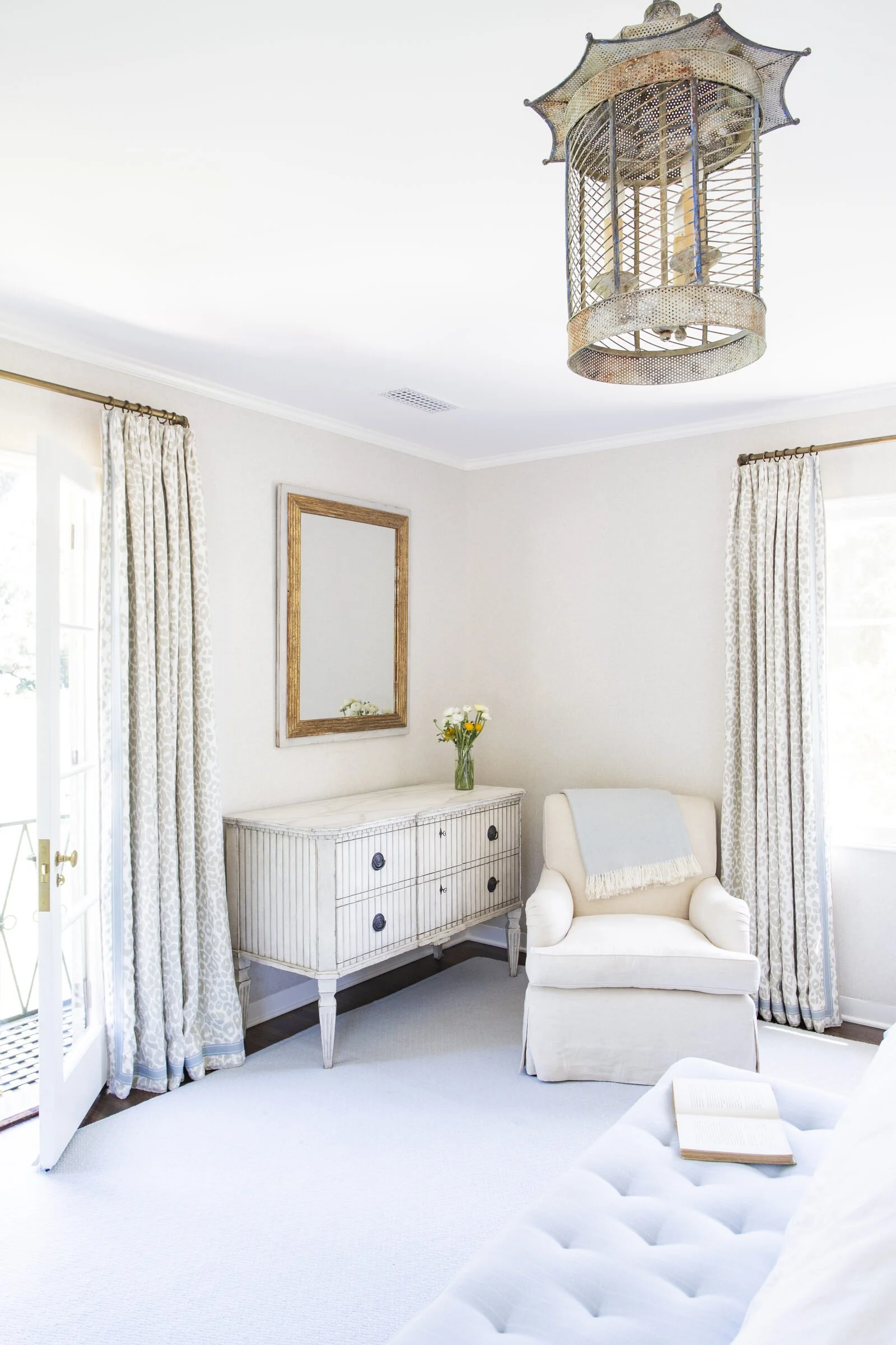 Nursery with a tufted white bench, a cream swivel chair, a Swedish-style dresser, a gilt mirror and leopard-print curtains