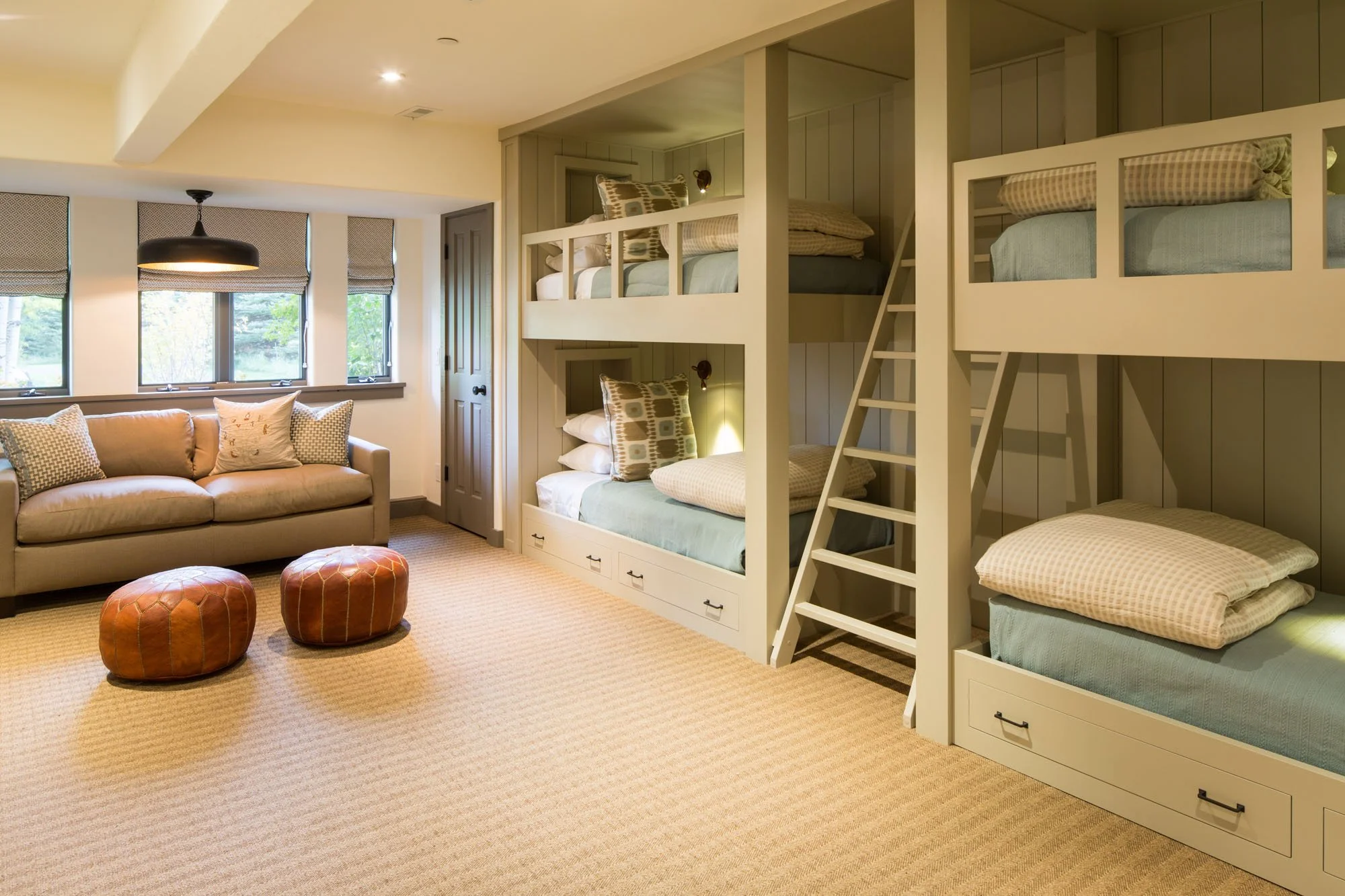 Bunk room with built-in bunk beds, a ladder, leather poufs and a sofa