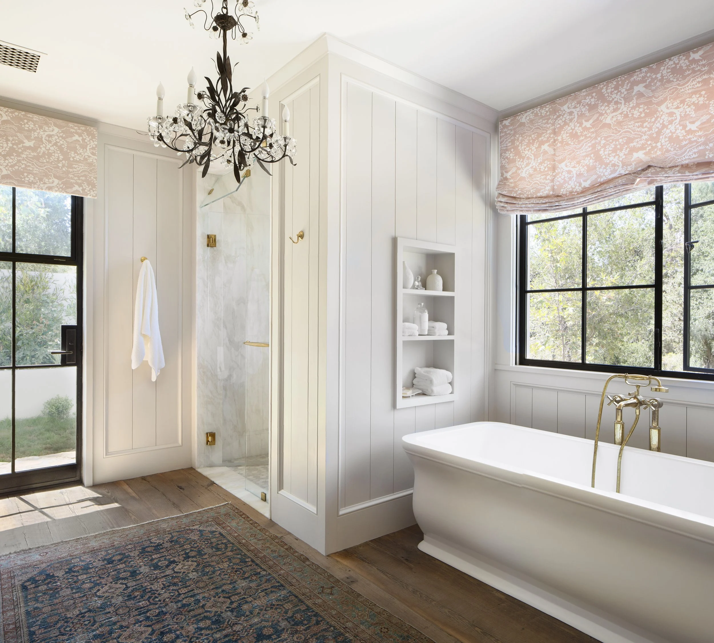 Bath with a freestanding tub, glass shower, steel-framed window and chandelier