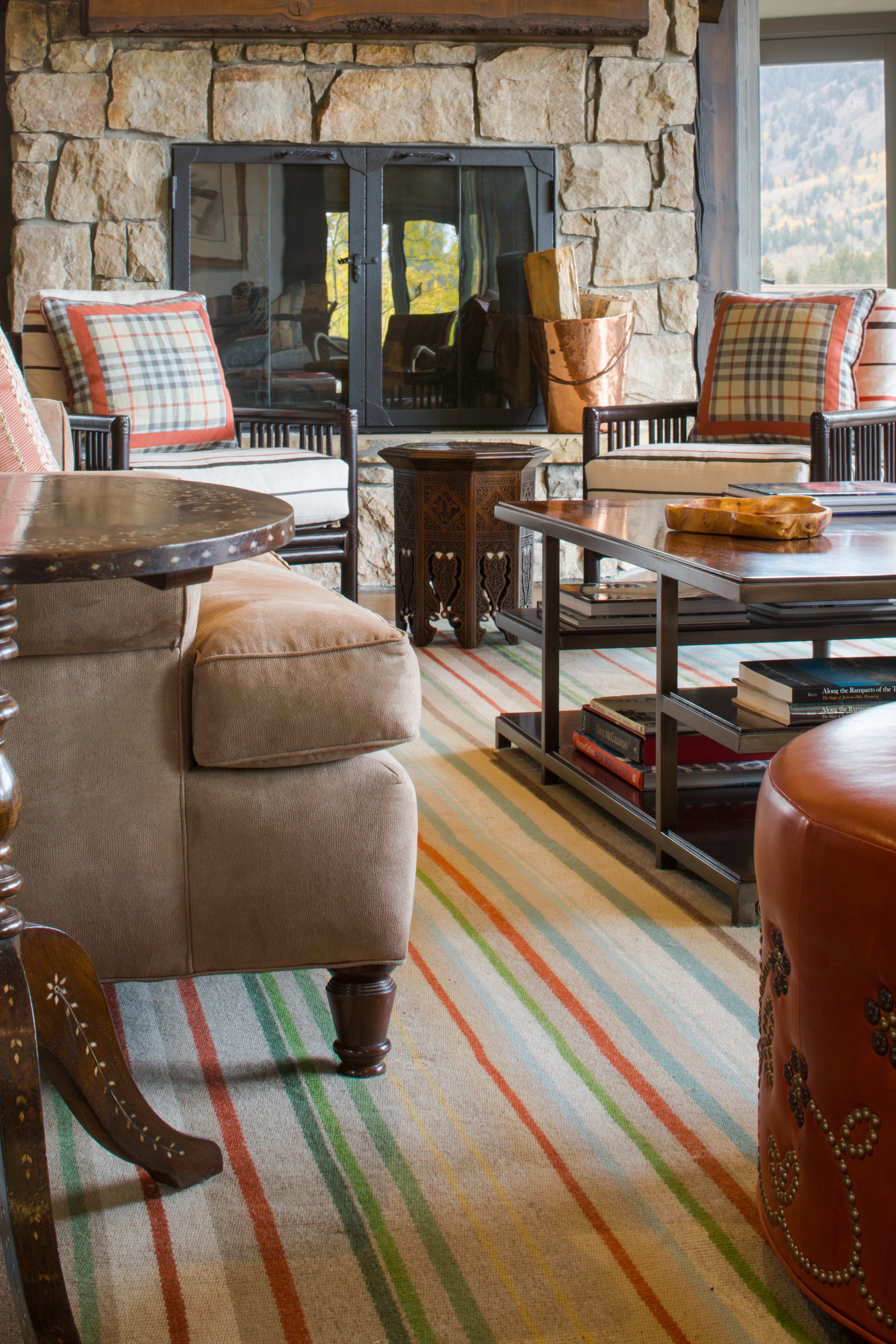 Close view of a tan upholstered chair, a leather ottoman and a striped rug beside a dark wood coffee table