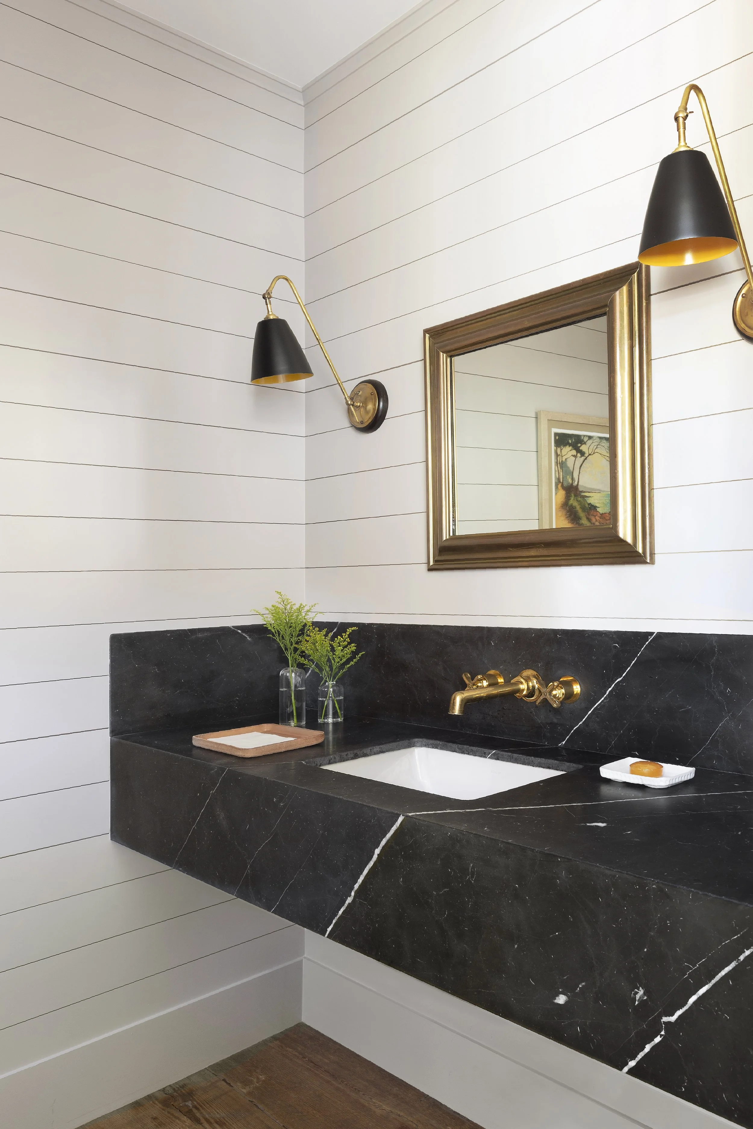 Powder room with shiplap walls, a black stone vanity, brass faucet and gilded mirror
