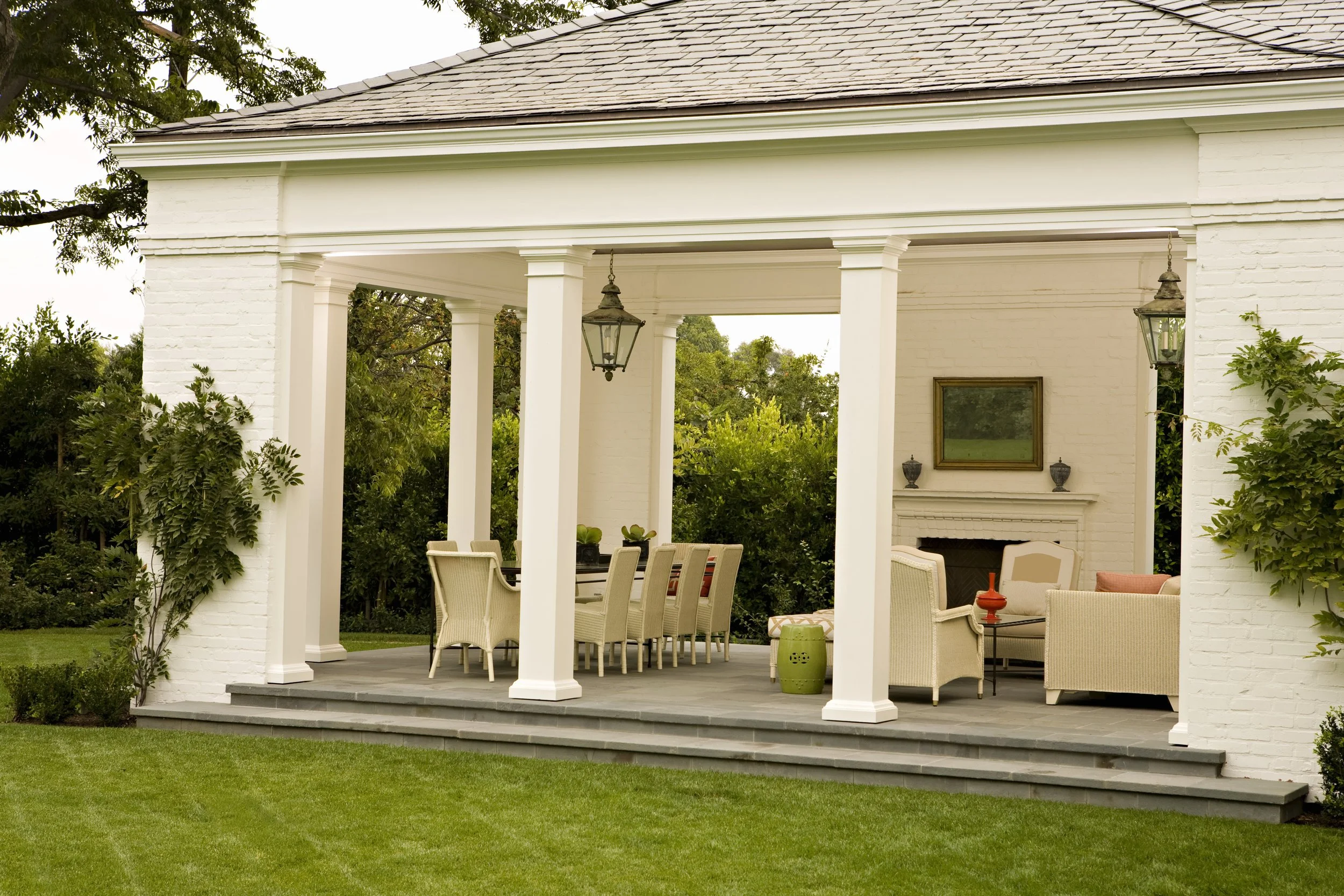 White columned pavilion with outdoor dining and a fireplace on a green lawn