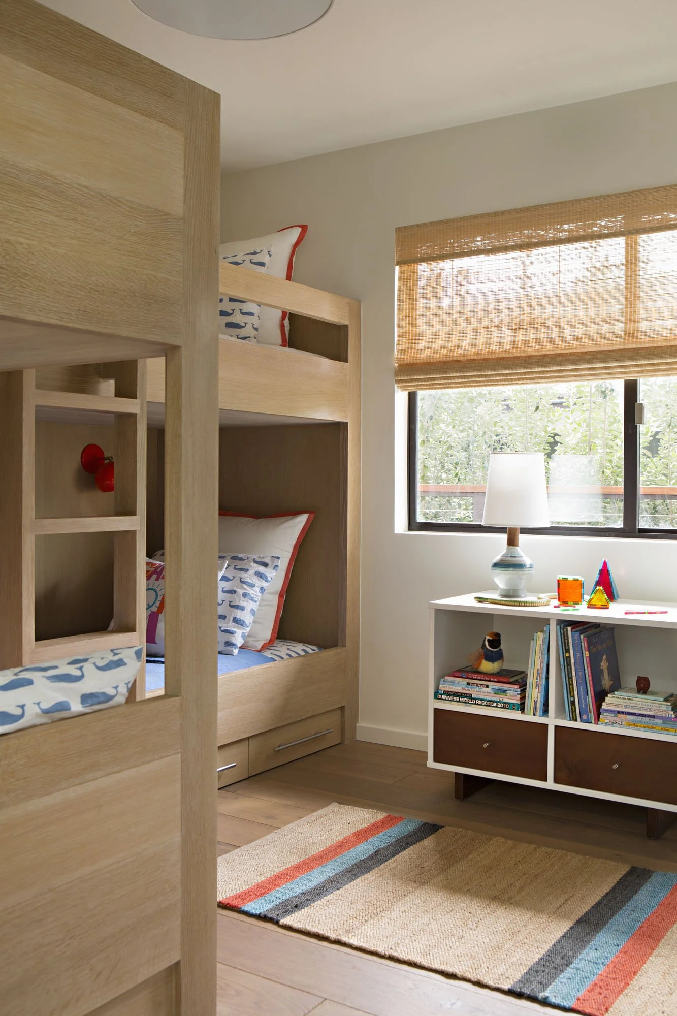 Child's bedroom with built-in oak bunk beds, bamboo shades, a bookshelf and whale-print bedding