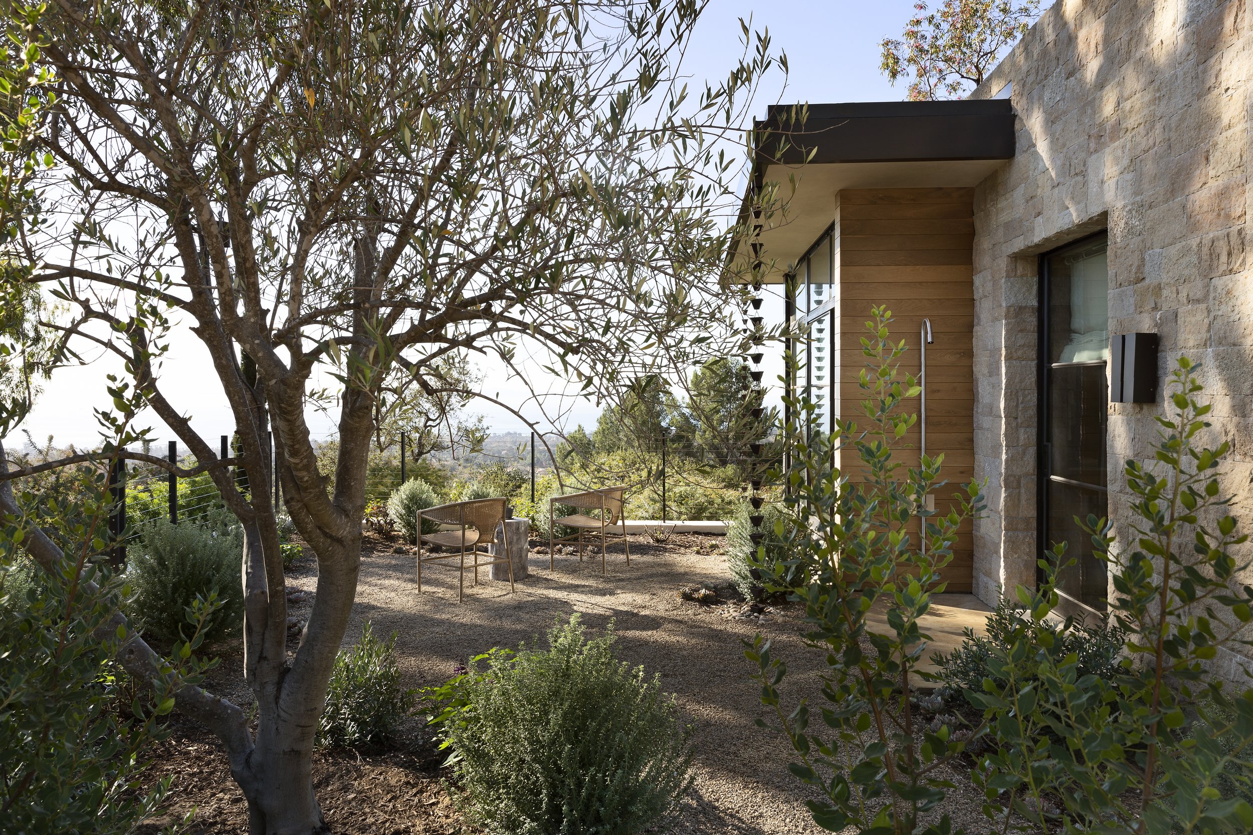 Garden courtyard with olive trees beside a stone and wood wing of the house
