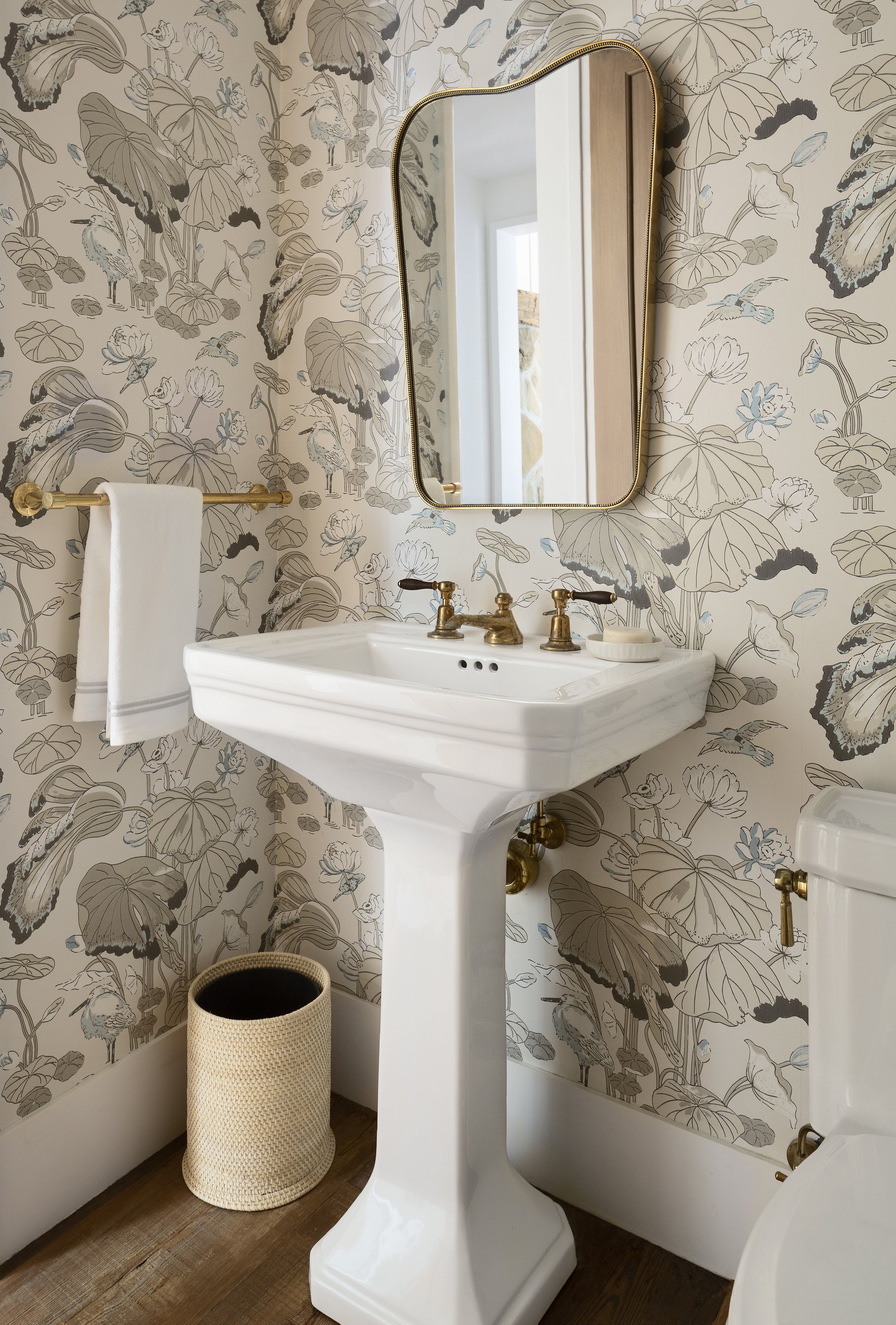 Powder room with botanical wallpaper, white pedestal sink and brass fixtures