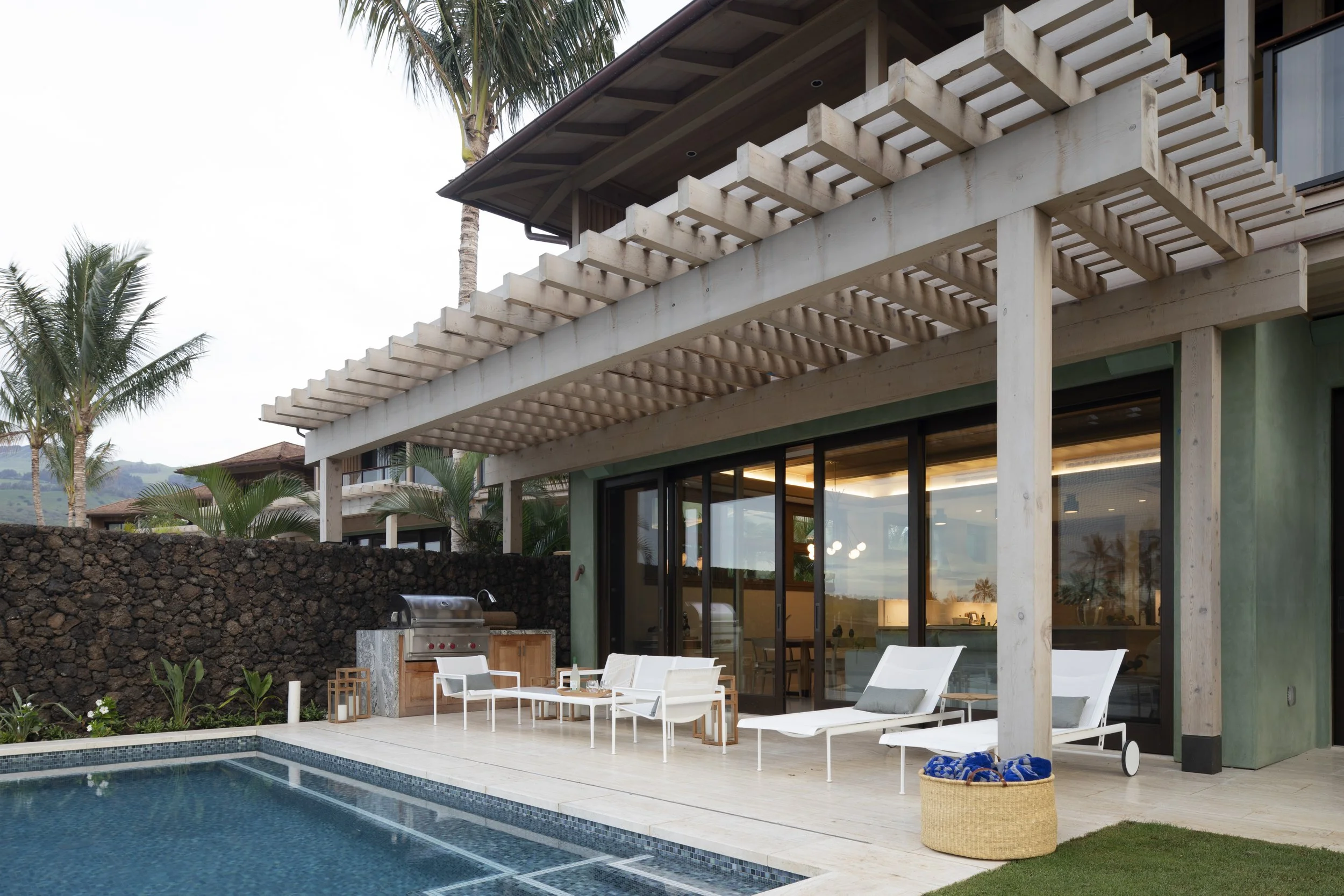 Pool terrace with a timber pergola, lounge chairs and a lava rock wall
