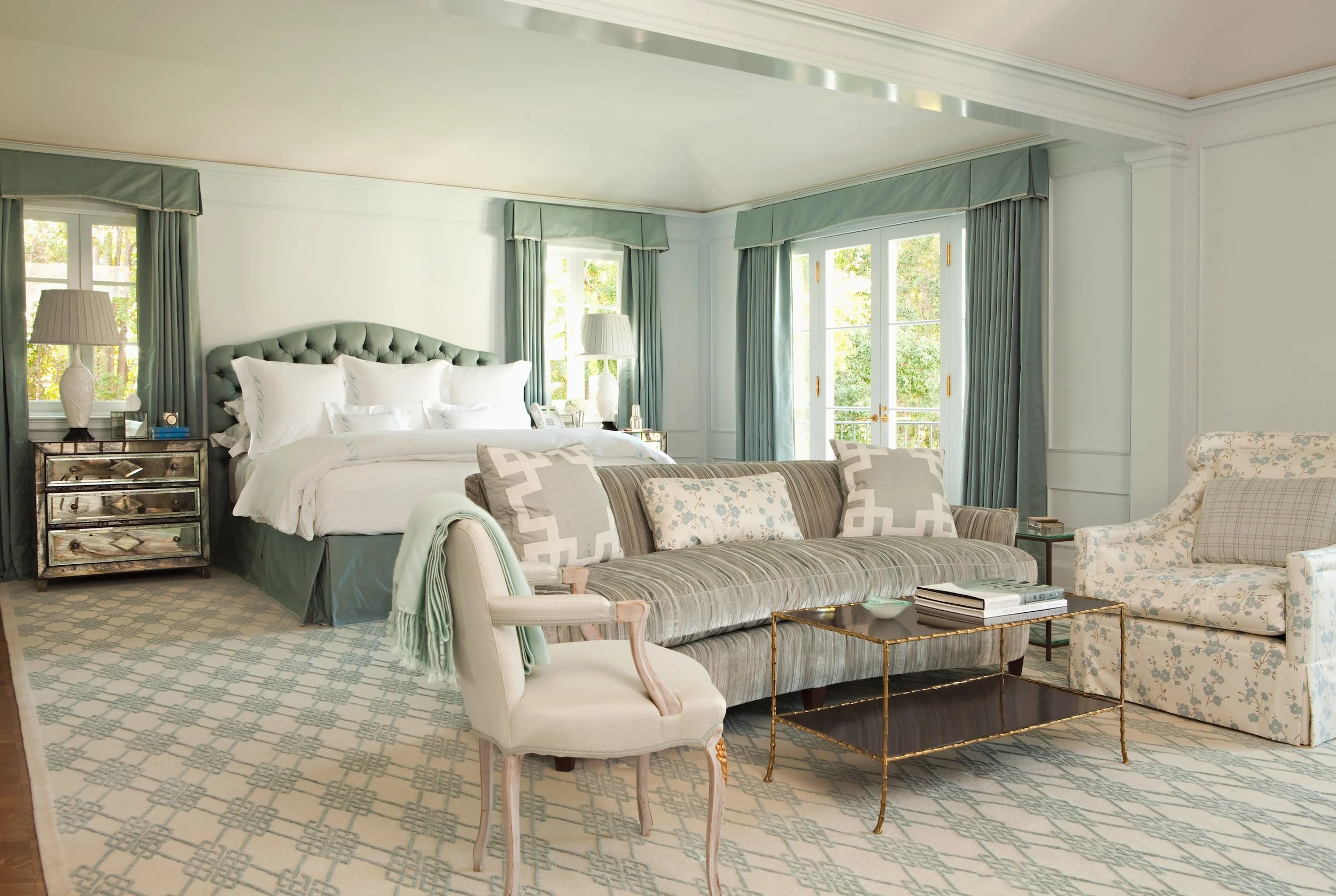 Primary bedroom with a tufted celadon headboard, mirrored nightstands and a curved sofa