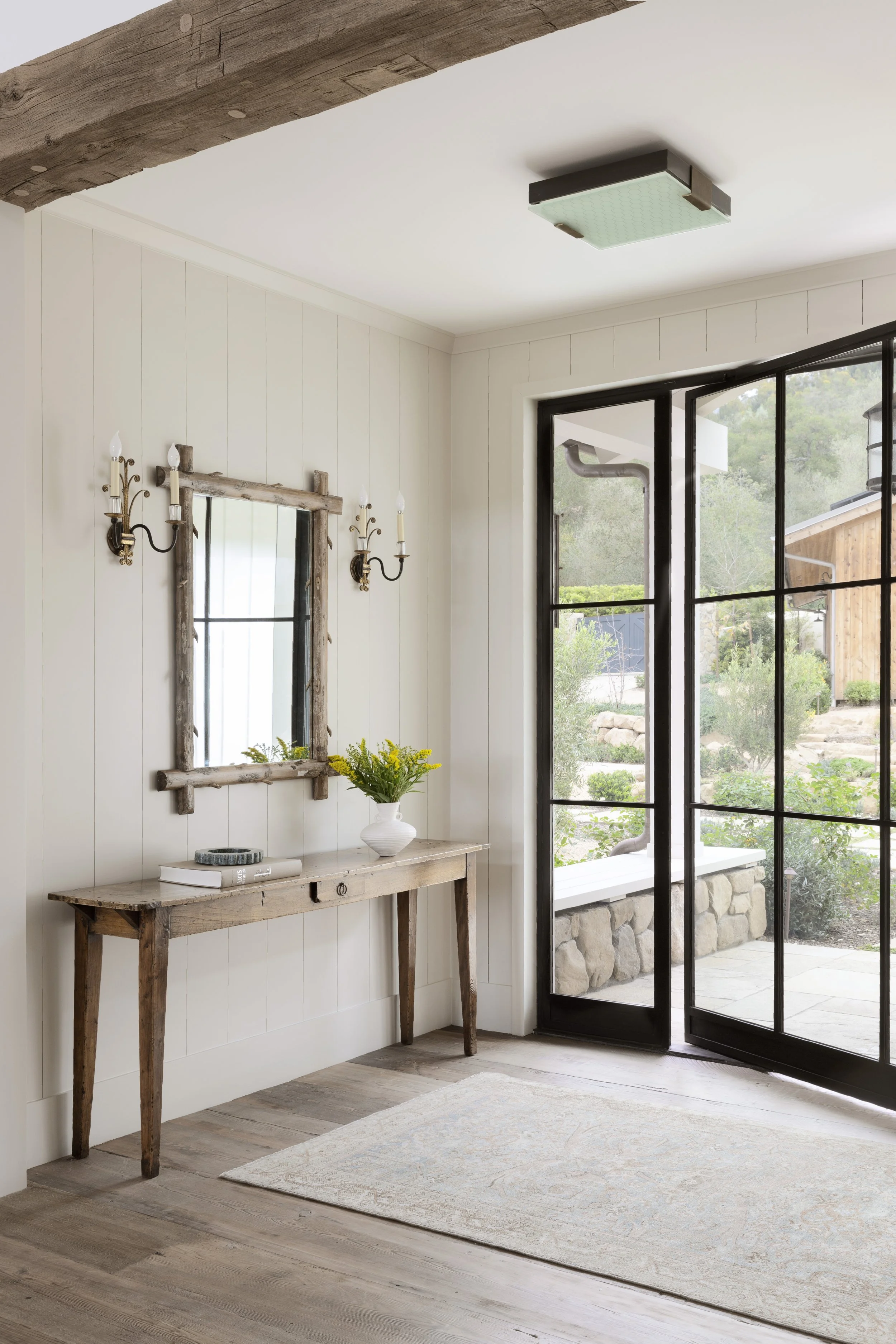 Entry console with a rustic wood mirror, sconces and steel-framed glass doors
