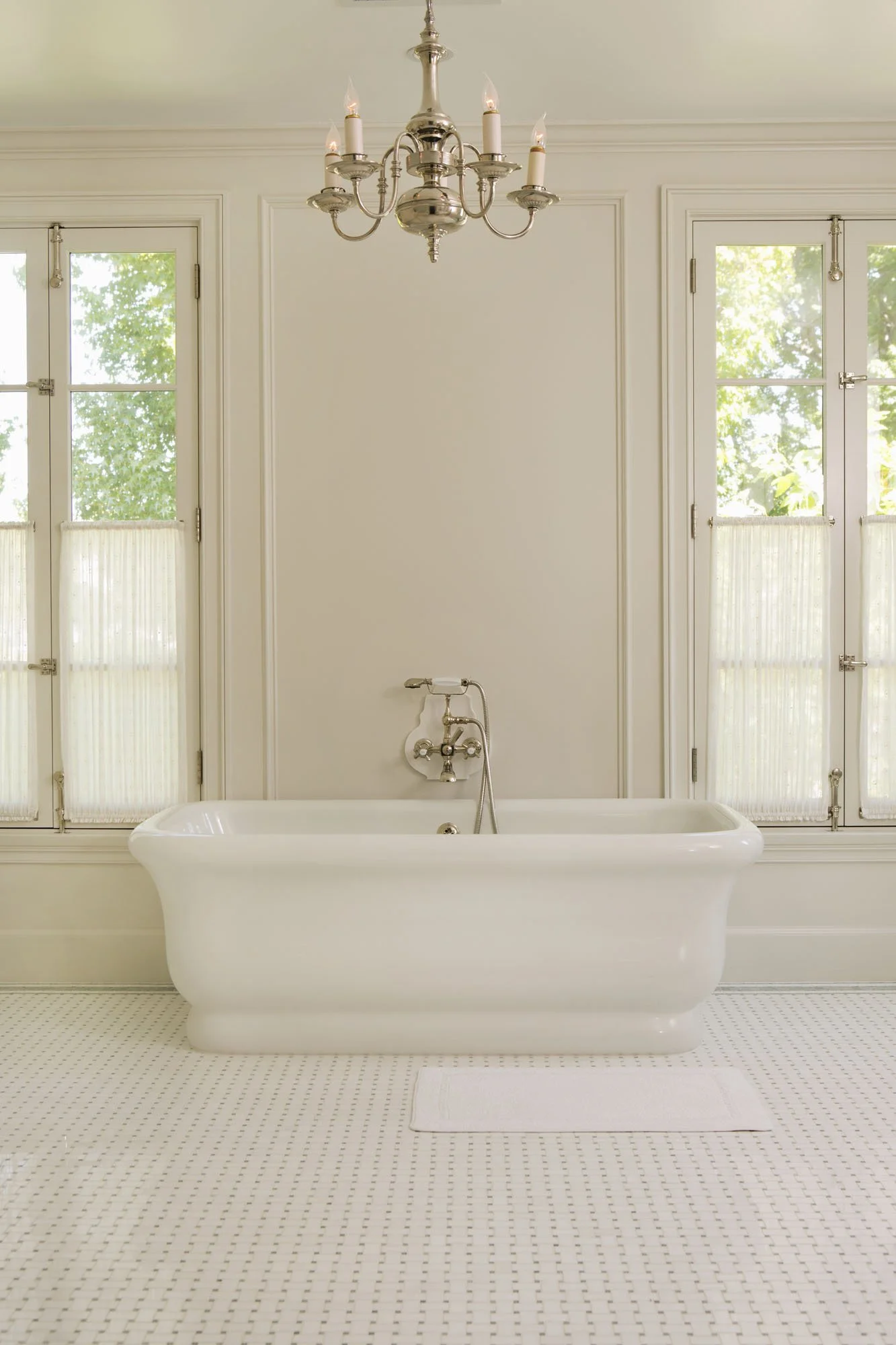 Freestanding white tub between tall French windows with a polished nickel tub filler