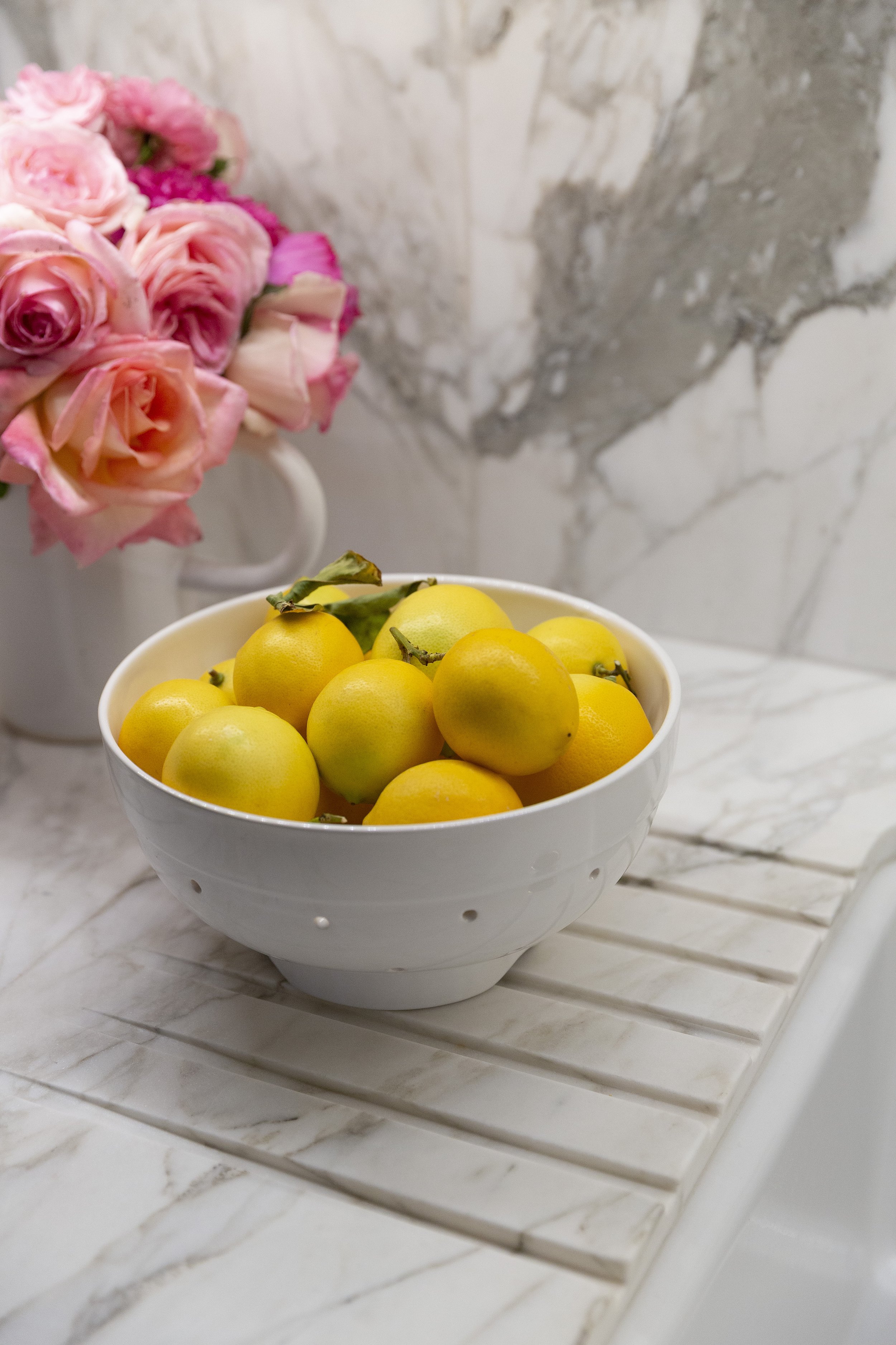 Bowl of lemons on a marble counter beside pink roses