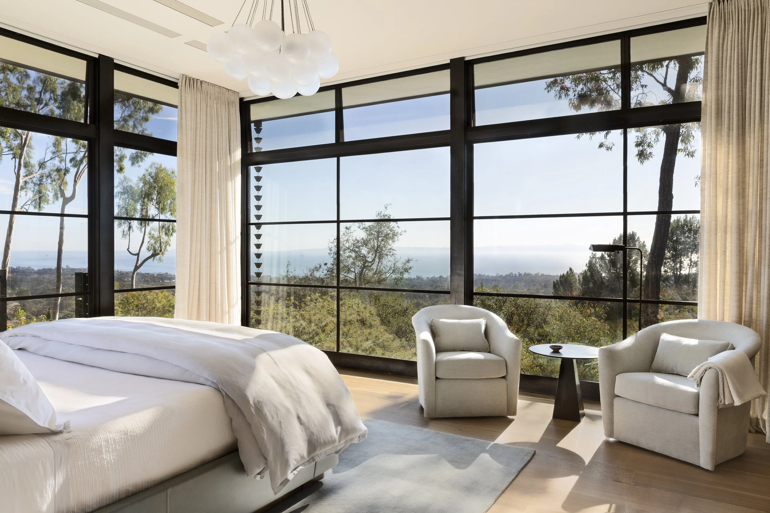 Primary bedroom with floor to ceiling windows facing the trees and a cloud pendant